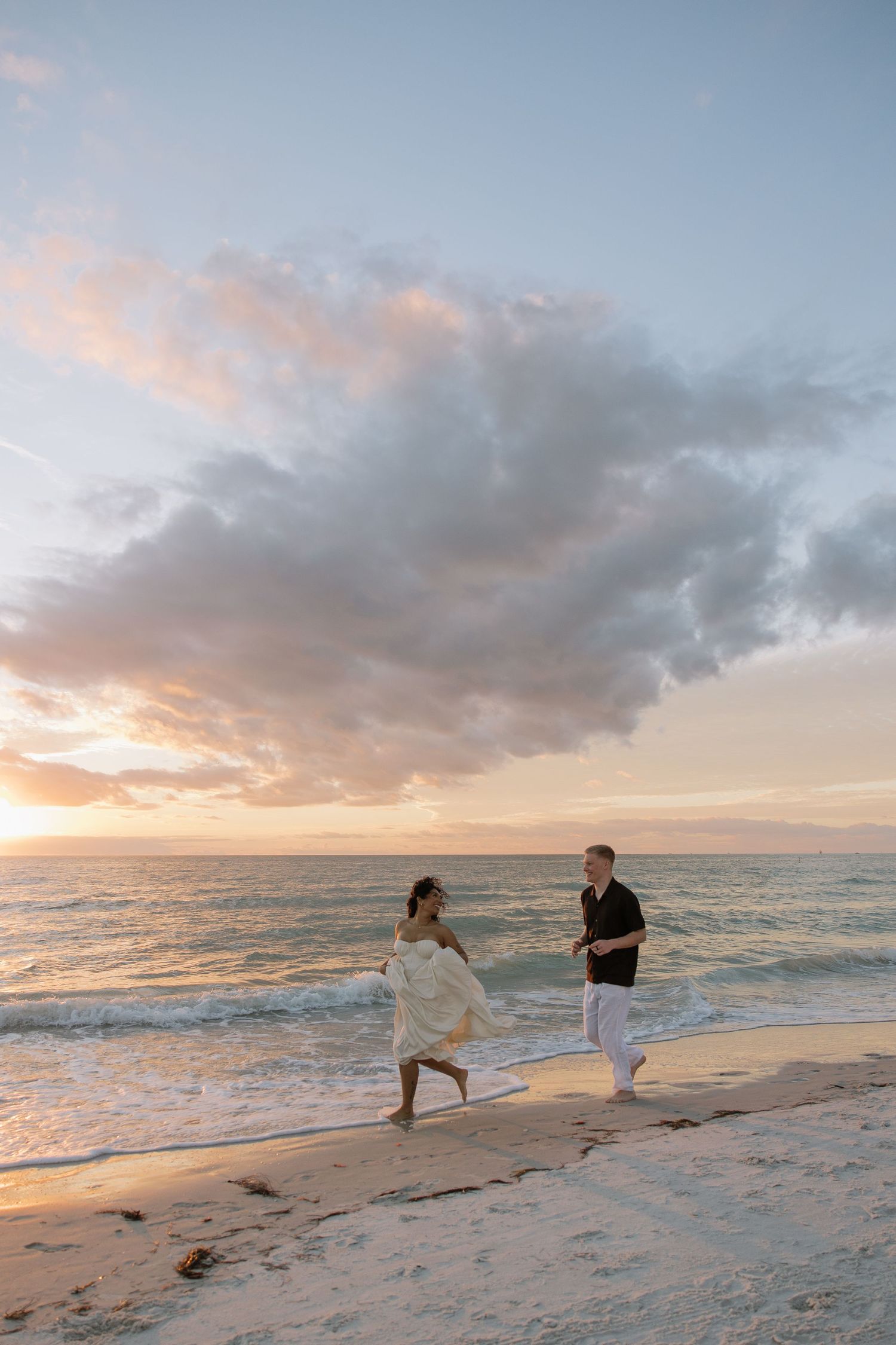 A engaged Tampa couple are running alongside Indian Rocks beach during golden hour captured by Michaela Gom Photography.