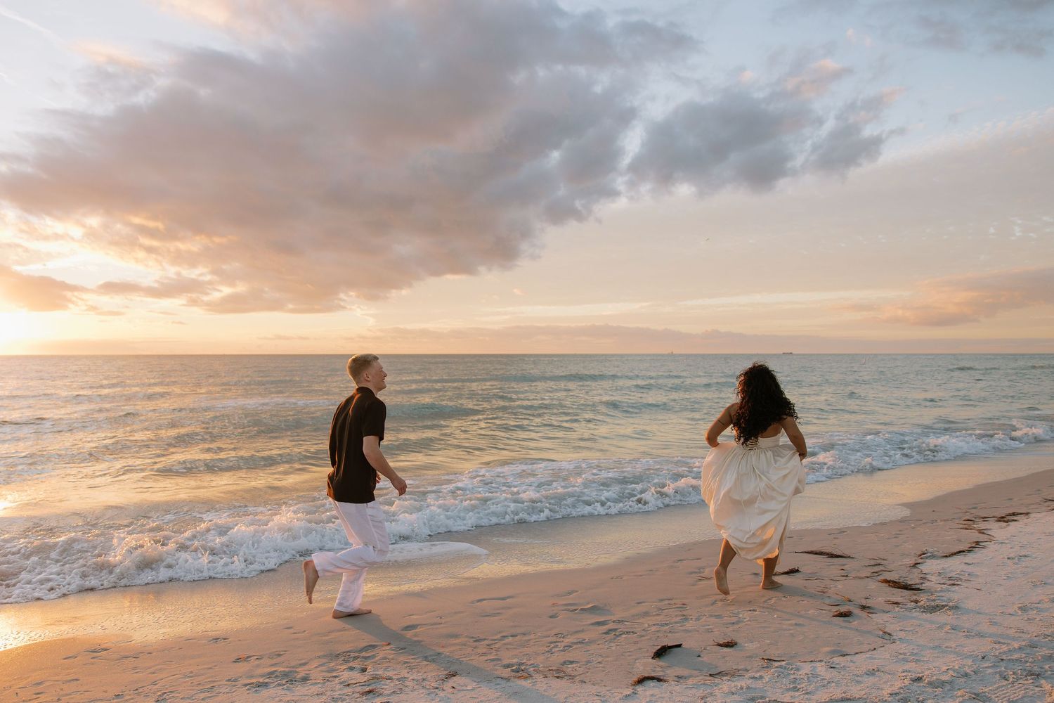 A engaged Tampa couple is running down the beach on Indian Rocks beach during golden hour captured by Michaela Gom Photography.