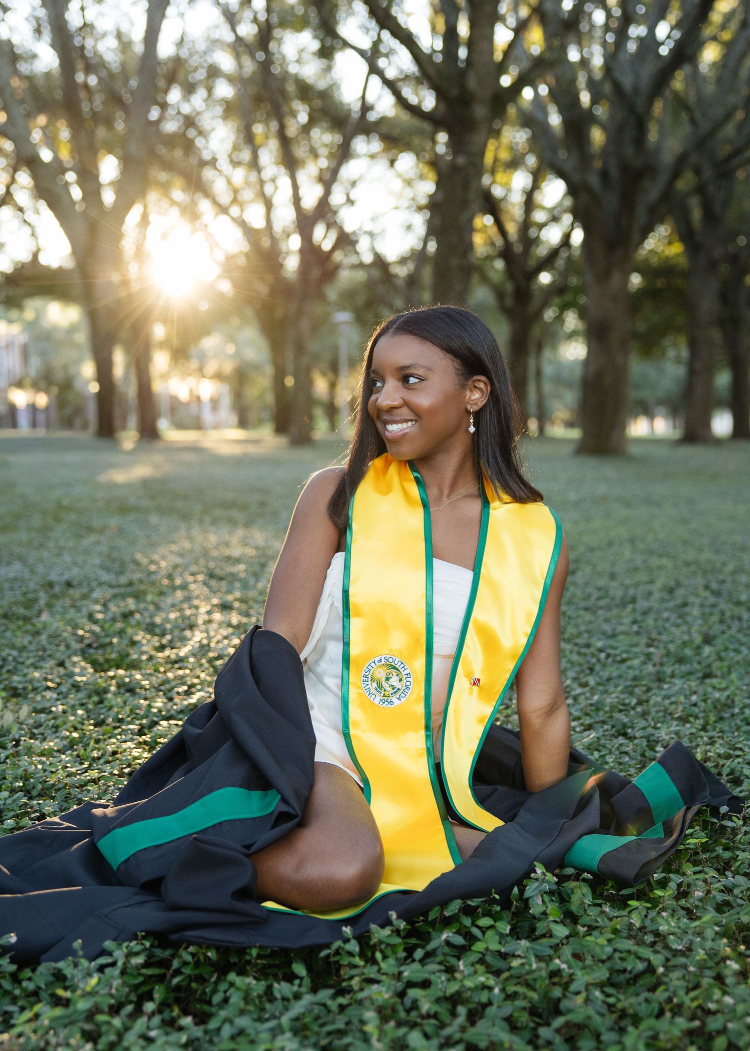A University of South Florida lays in grass posing for her grad photos at captured by Tampa grad photographer Michaela Gom Photography.