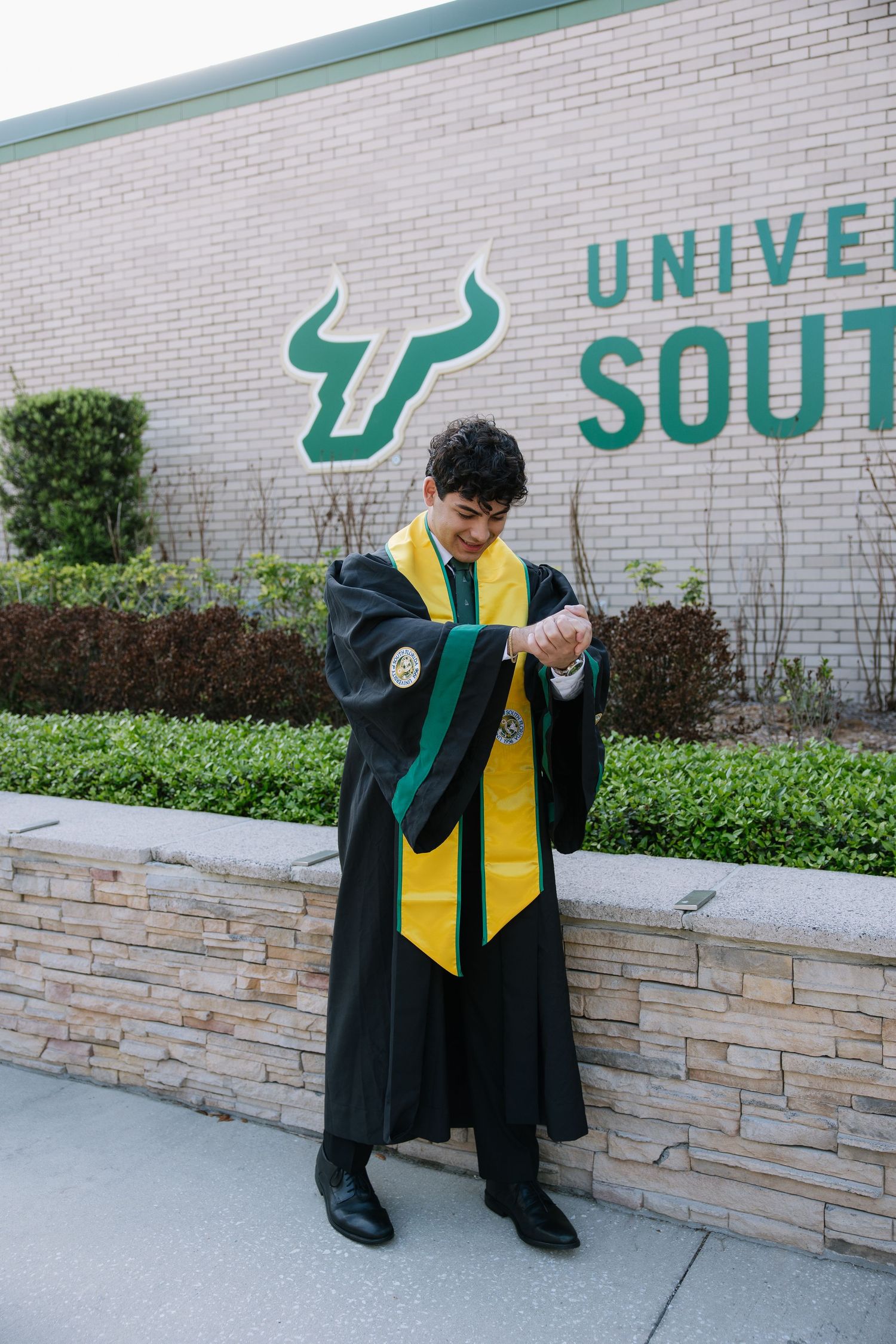 USF grad stands in front of the USF sign for his graduation photos taken by Michaela Gom Photography.