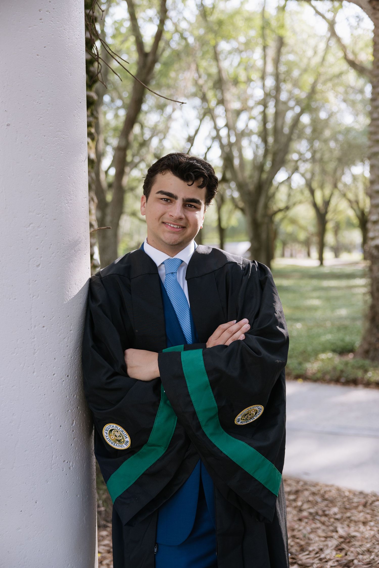 A University of South Florida grad stands by the pillar wearing his regalia captured by Tampa grad photographer Michaela Gom Photography.
