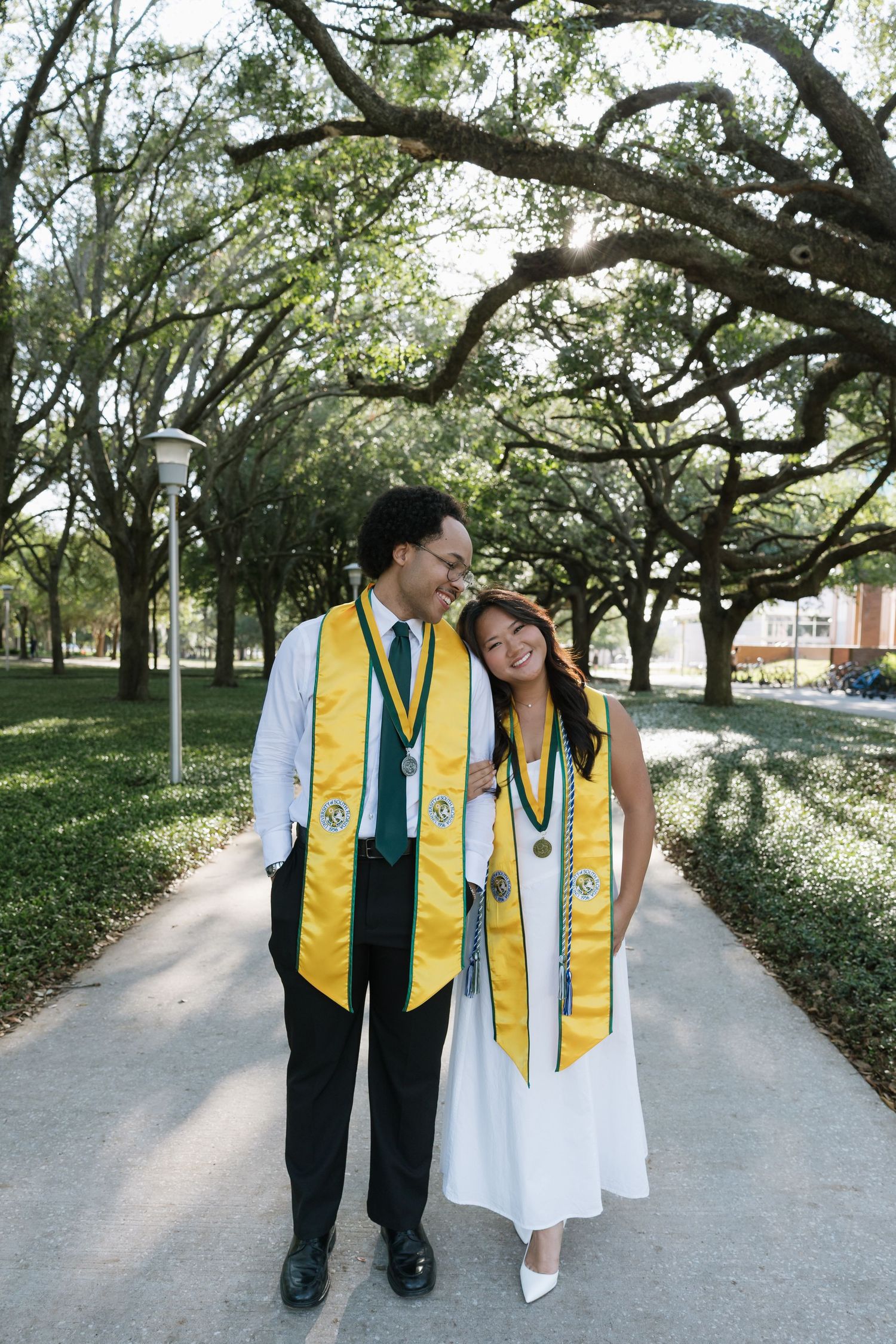Two USF grad students are standing holding arms and smiling for their graduation photos taken by Michaela Gom Photography.