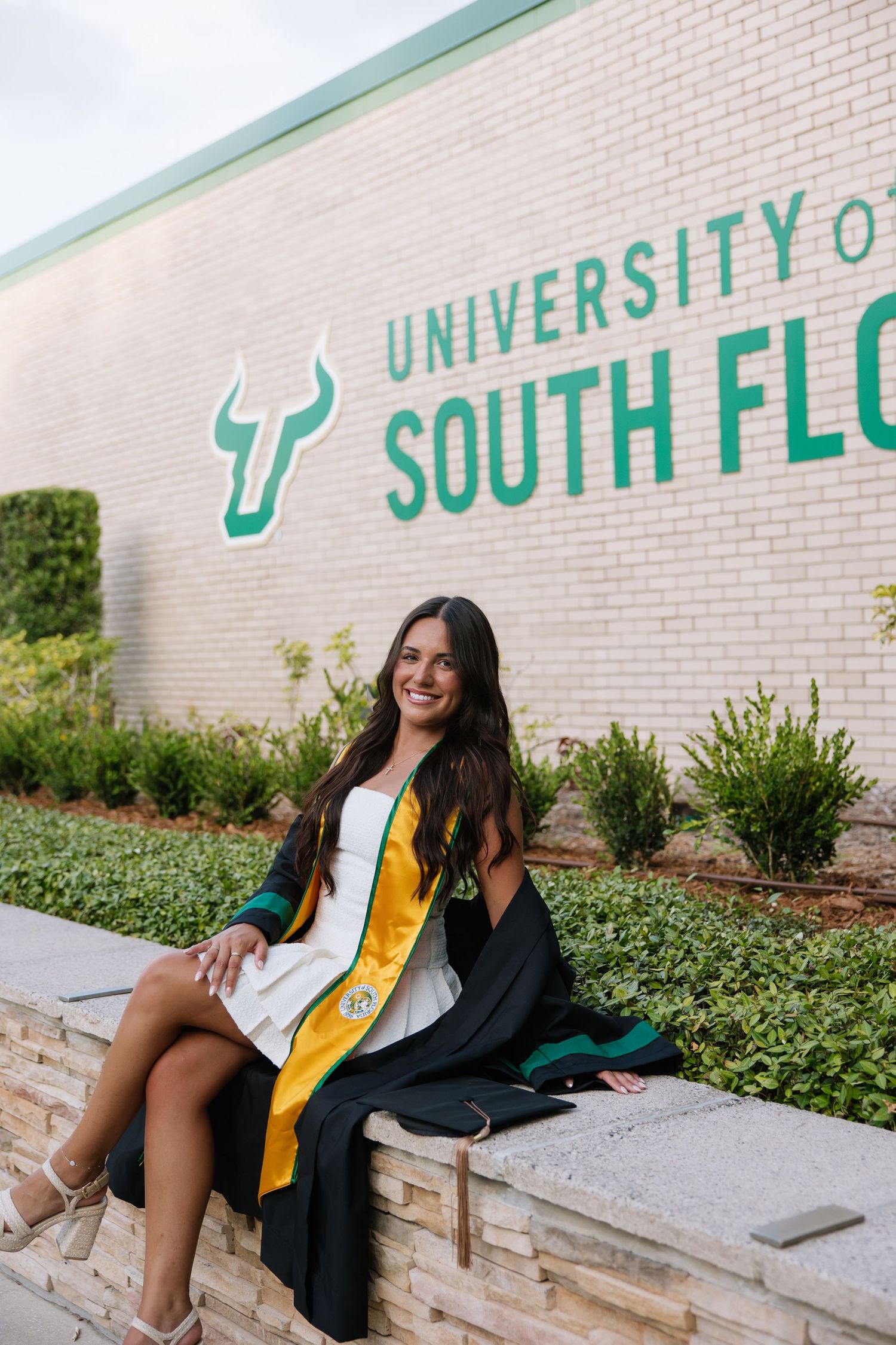 A University of South Florida grad poses in front of the USF sign shot by photographer Michaela Gom Photography.