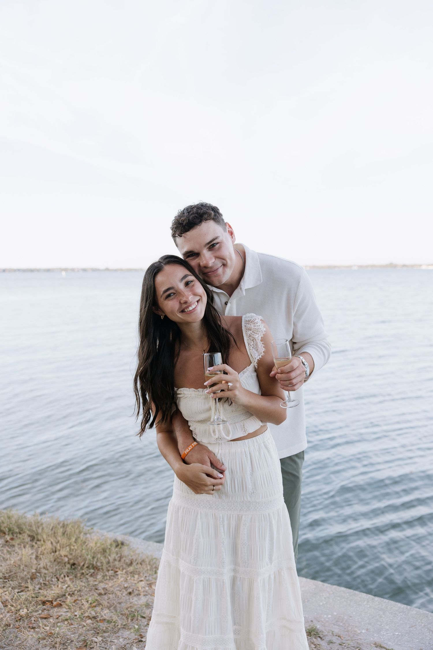 Engaged couple looks stands together holding champagne glasses captured by timeless true to color photographer Michaela Gom Photography.