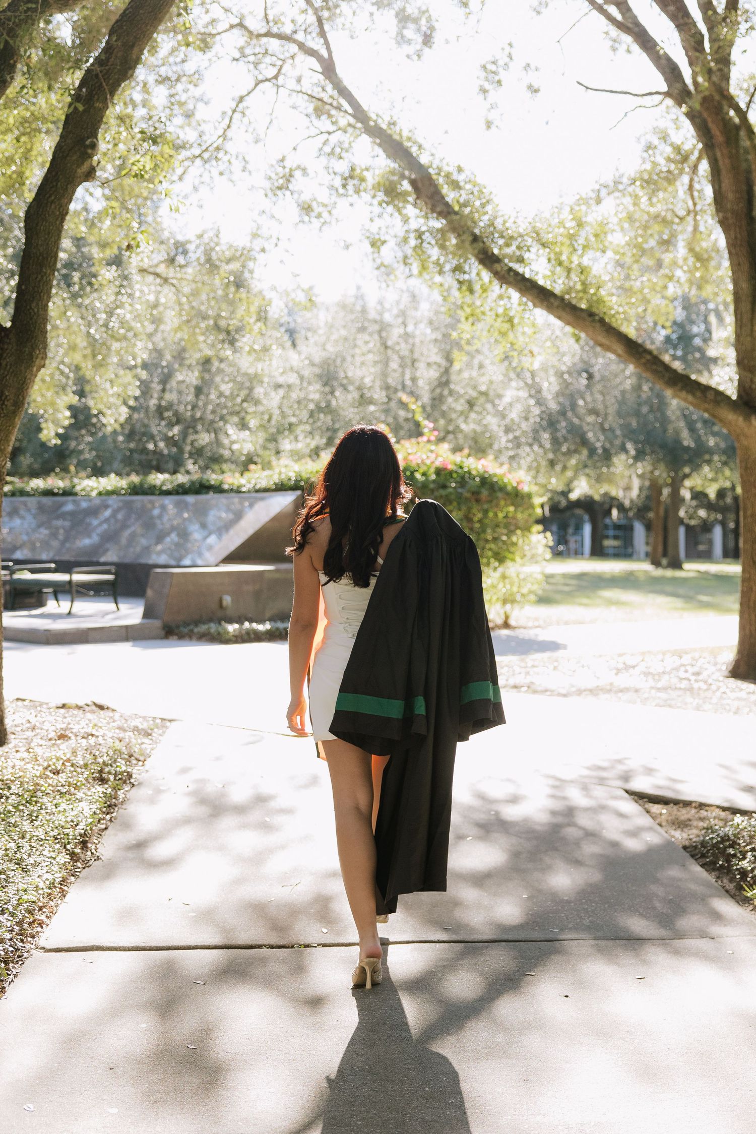 A University of South Florida graduate holds her gown and walks away taken by Tampa grad photographer Michaela Gom Photography.