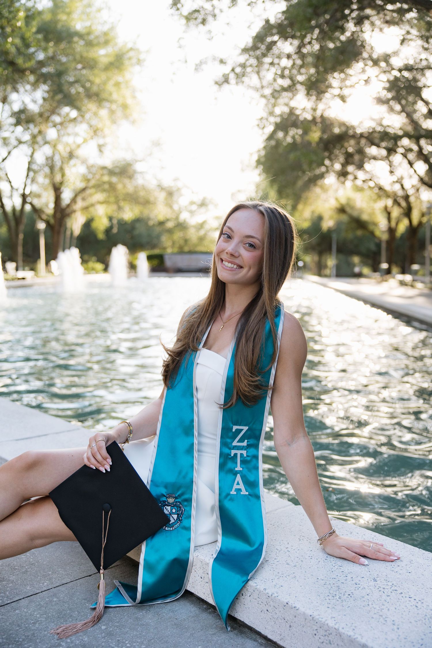 A University of South Florida graduate is sitting on the ledge of the MLKJr fountain by Tampa grad photographer Michaela Gom Photography.