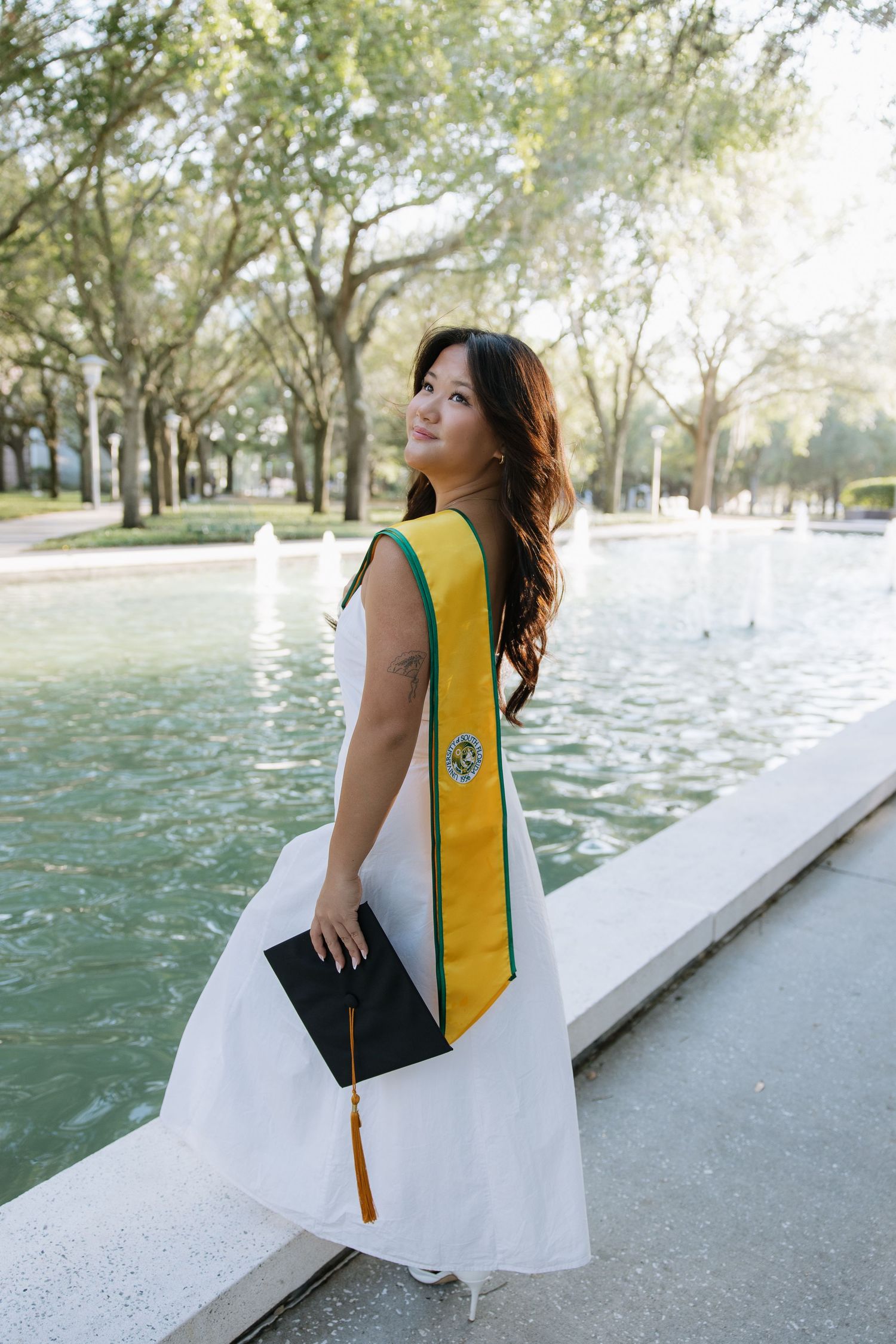 A USF grad holds her cap standing on the fountain captured by Tampa grad photographer Michaela Gom Photography.