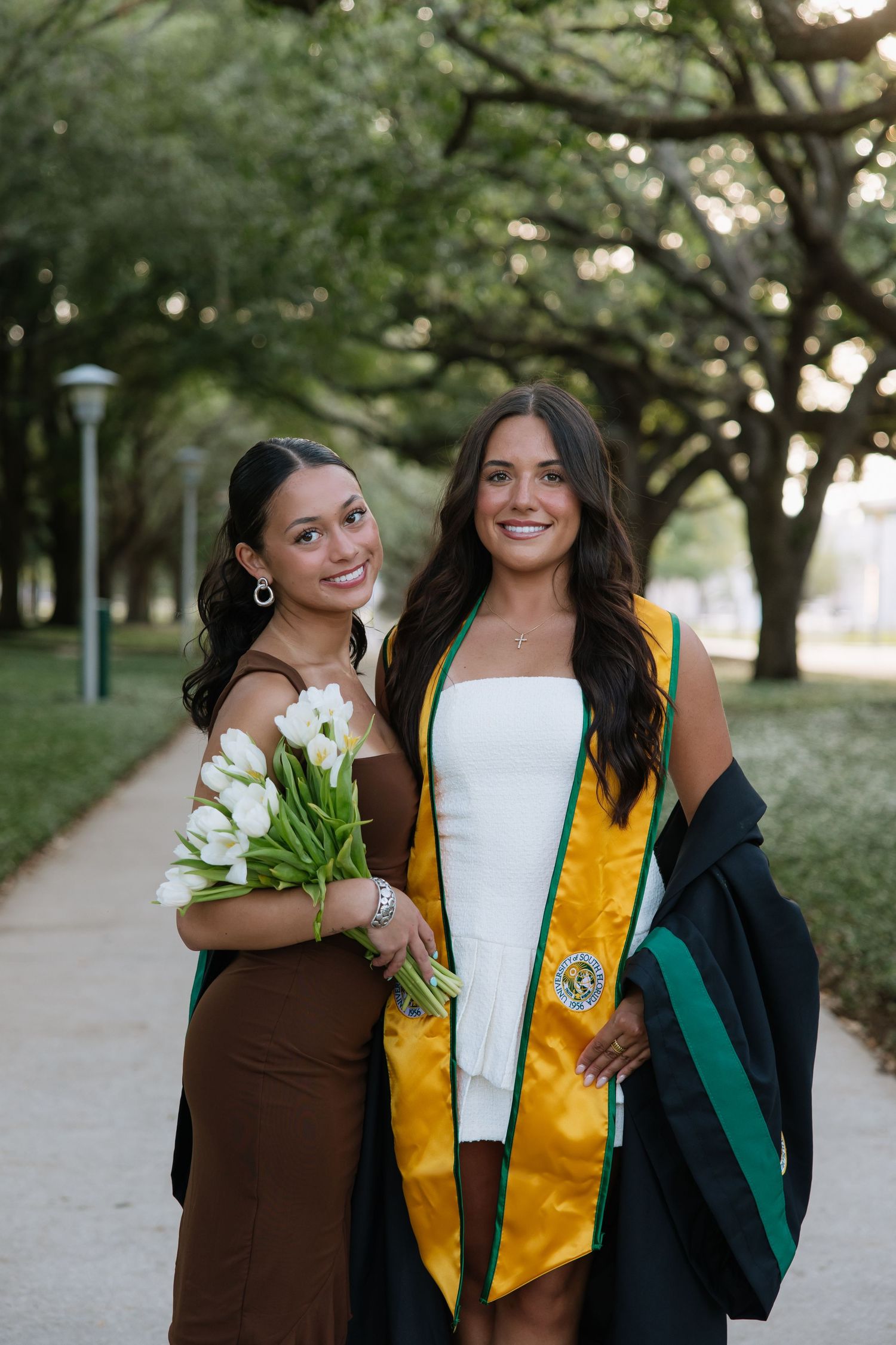 A University of South Florida graduate stands with her friend in her grad photos captured by Michaela Gom Photography.
