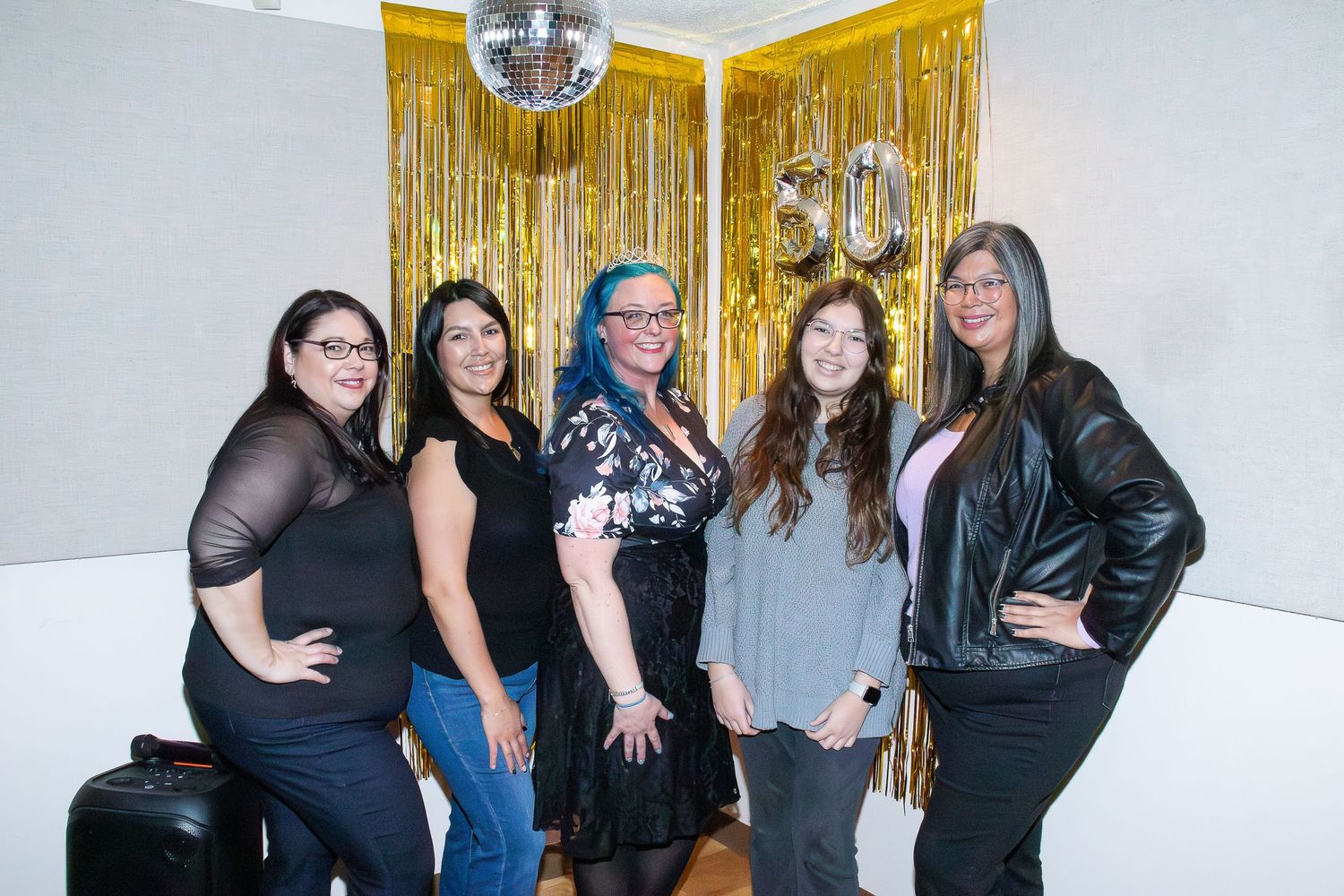 Group celebrates under gold fringe decorations and disco ball at indoor party.