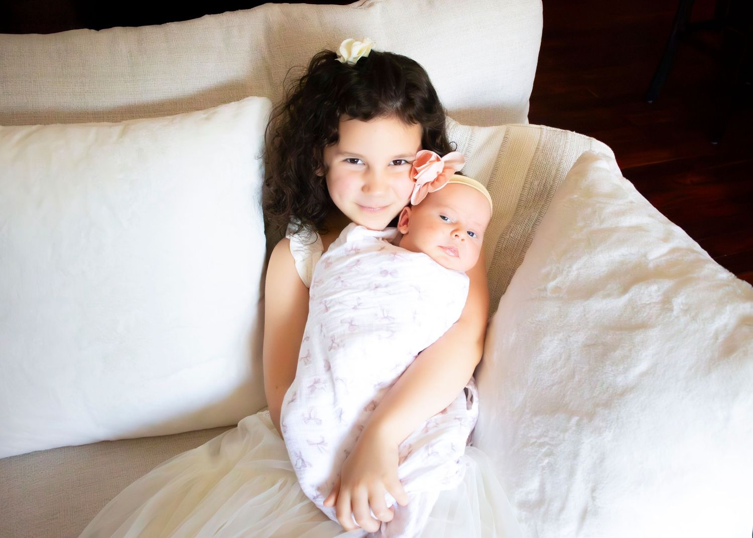 Baby dressed in white on white bedding in bright natural light.