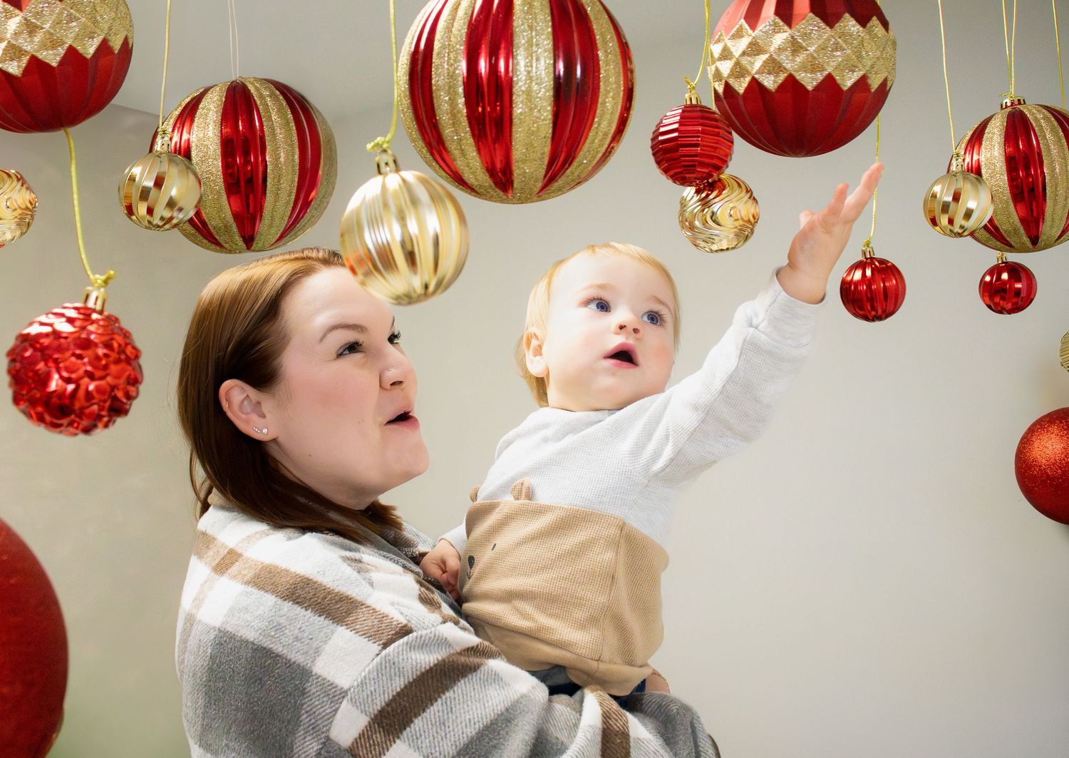 A joyful holiday scene with red and gold ornaments hanging from above as someone reaches toward the decorations.