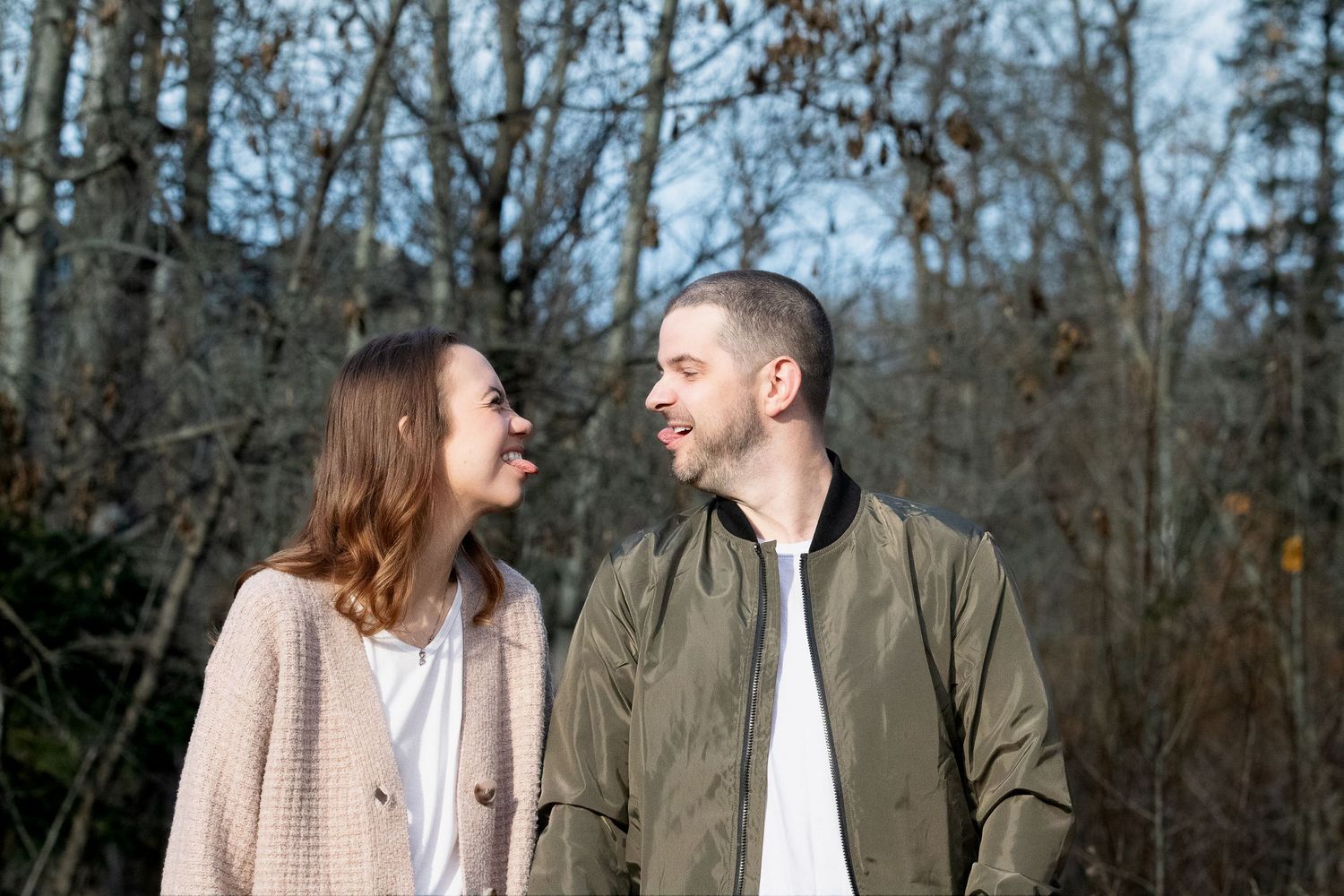 Two people in casual attire share a loving moment outdoors against a backdrop of bare trees in winter.