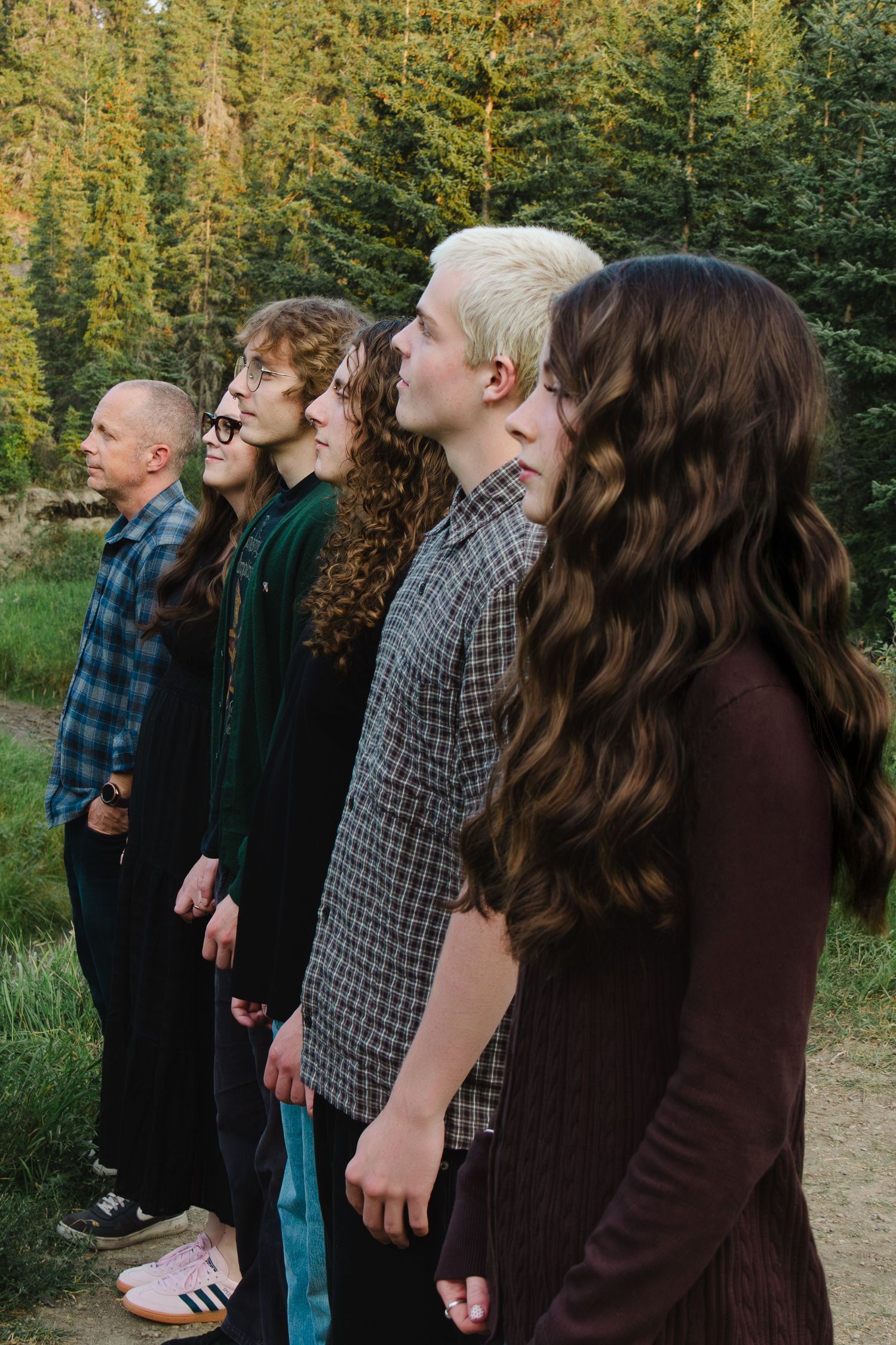 A group of people standing in a line outdoors with trees and greenery in the background.