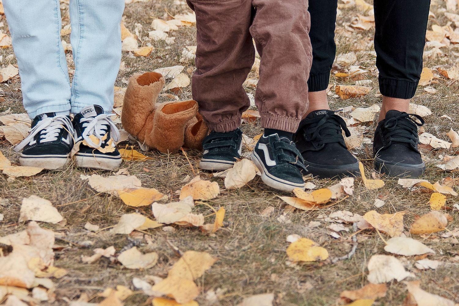 Group of people wearing casual shoes and jeans standing in fallen autumn leaves on the ground.