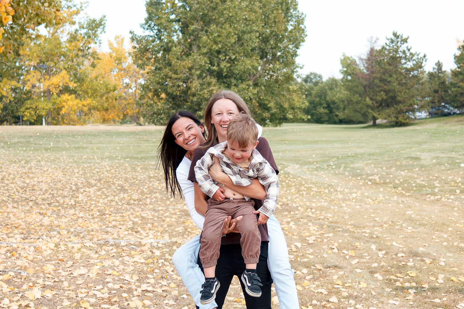 A group enjoys a playful autumn photoshoot outdoors with fallen leaves scattered on the ground.
