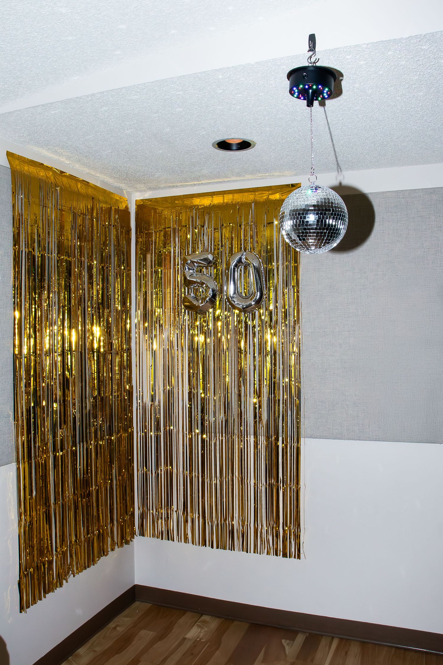 Room decorated with gold metallic fringe curtains and hanging disco ball for party.