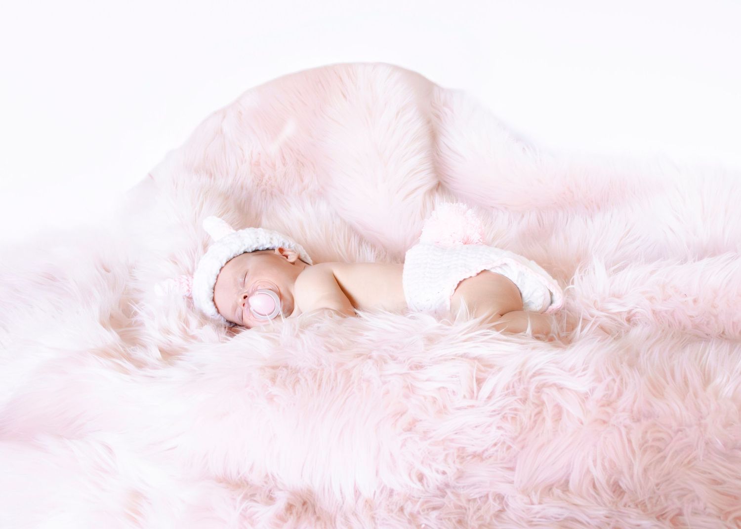 Artistic panoramic of baby sleeping on plush pink textured backdrop.
