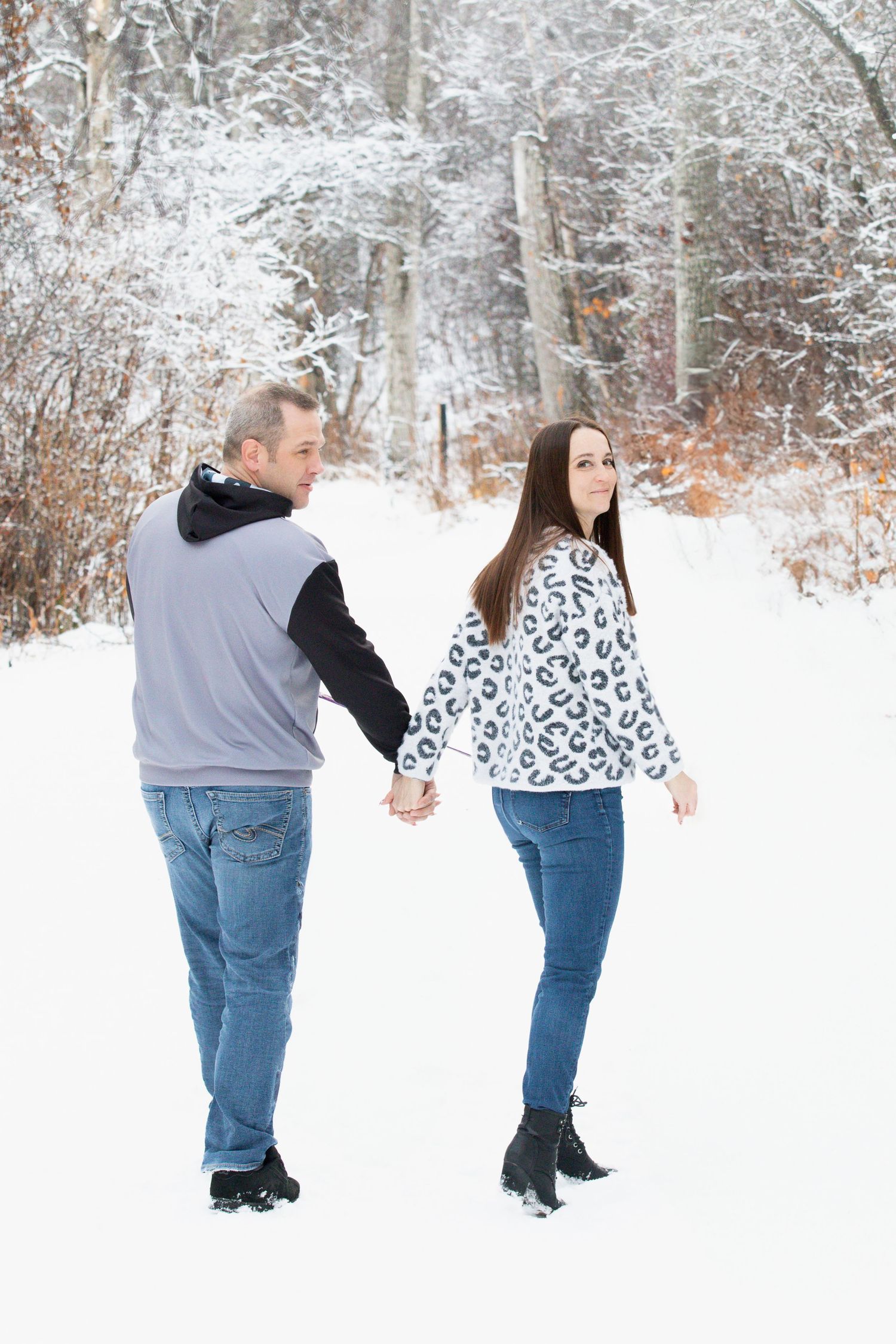 A couple holding hands while walking through a snowy winter landscape.