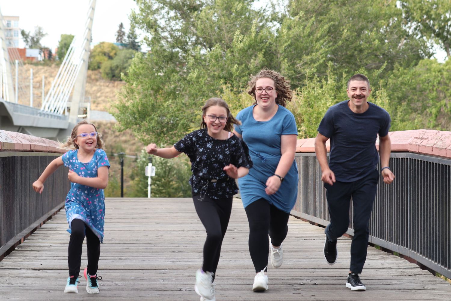 A family running and laughing together along a wooden bridge walkway in a park setting.