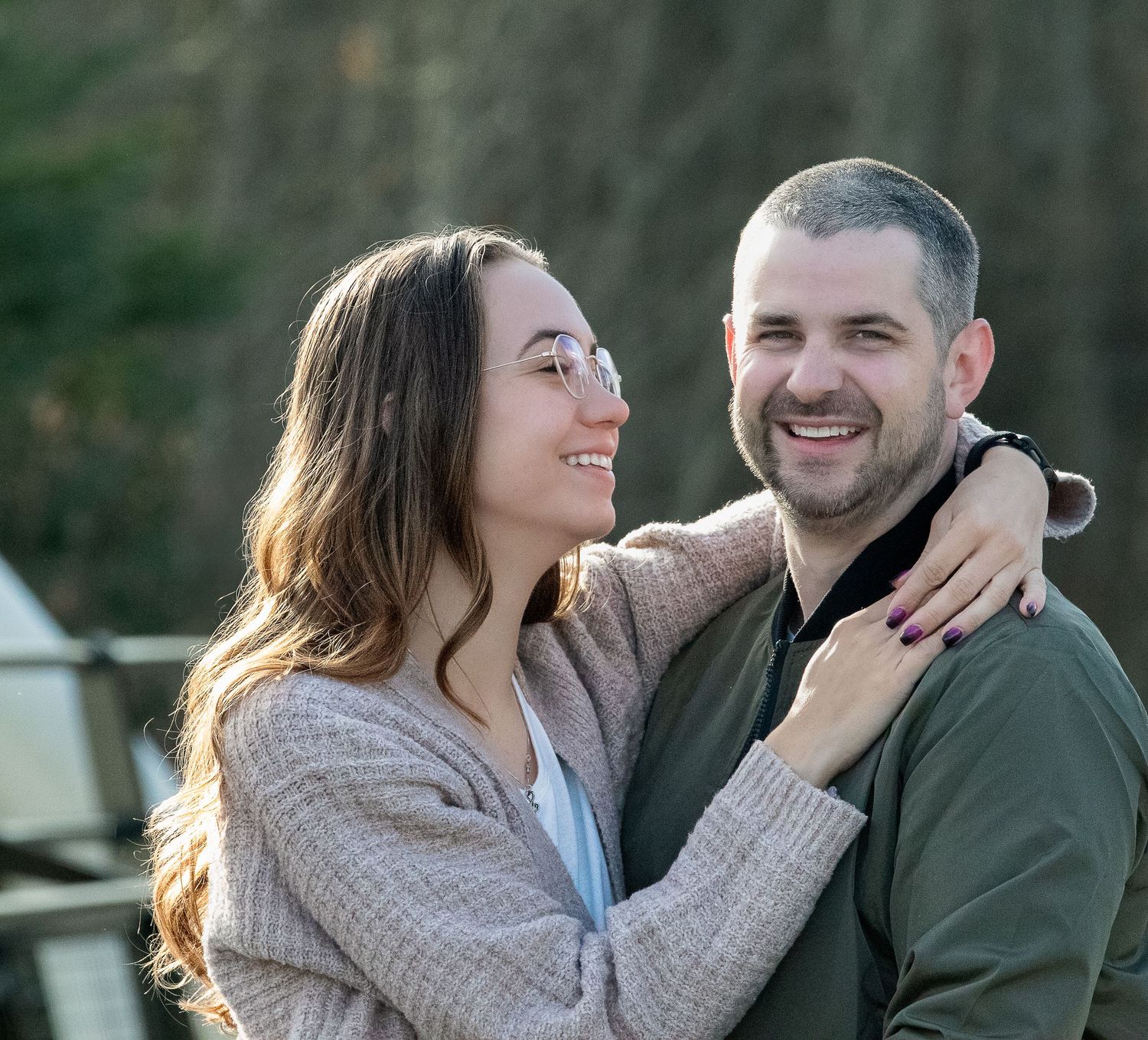 Loving couple embracing and laughing together outdoors on a sunny day wearing casual sweaters.