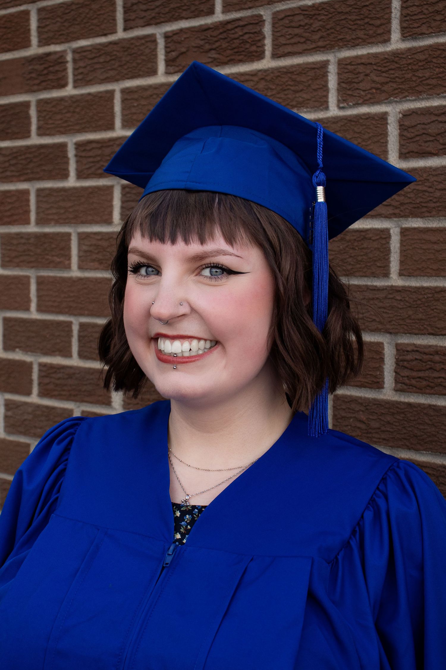 Graduate wearing royal blue cap and gown poses against brick wall background.
