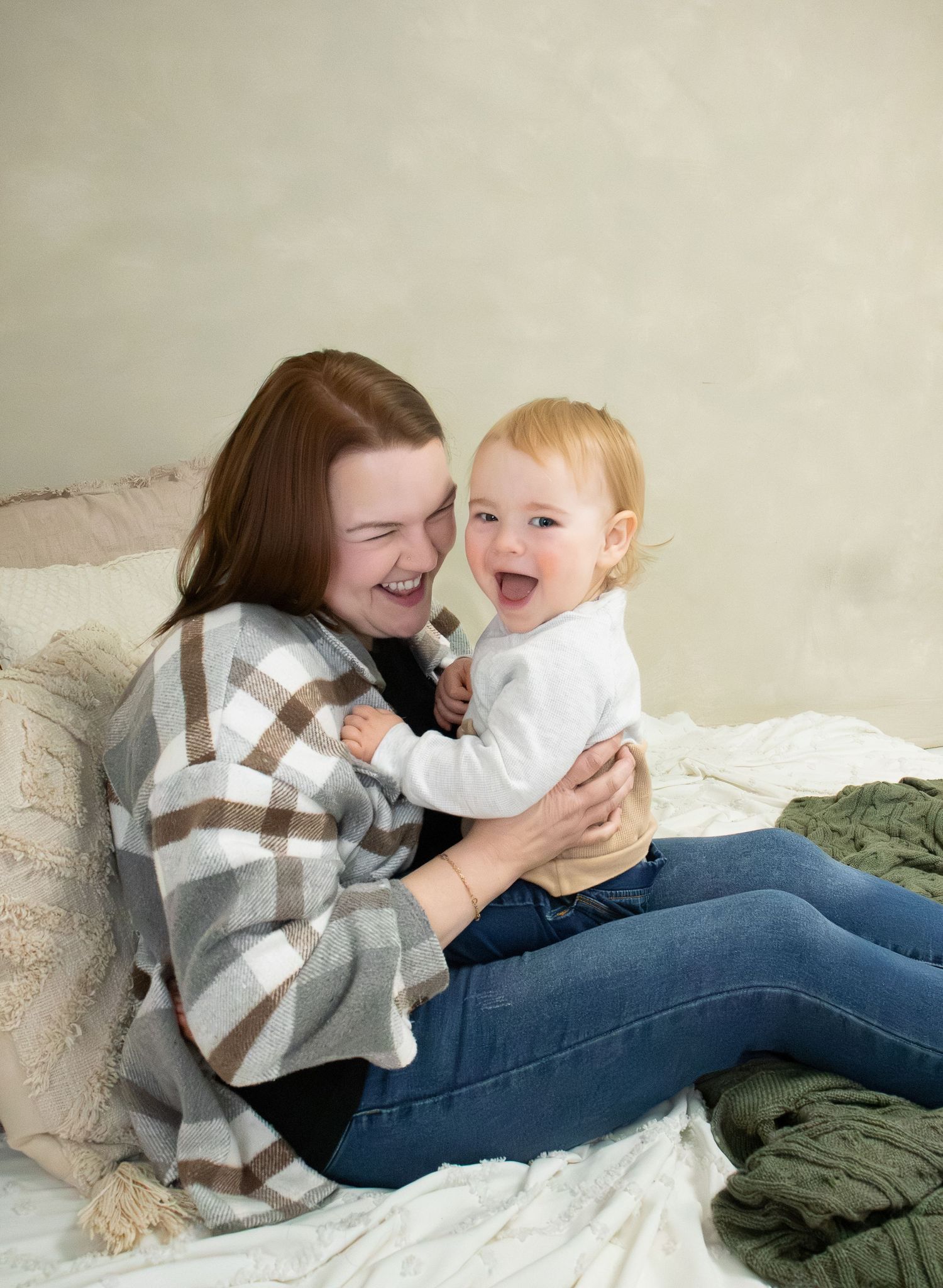 A heartwarming moment of laughter and bonding between adult and baby sitting together on white bedding.