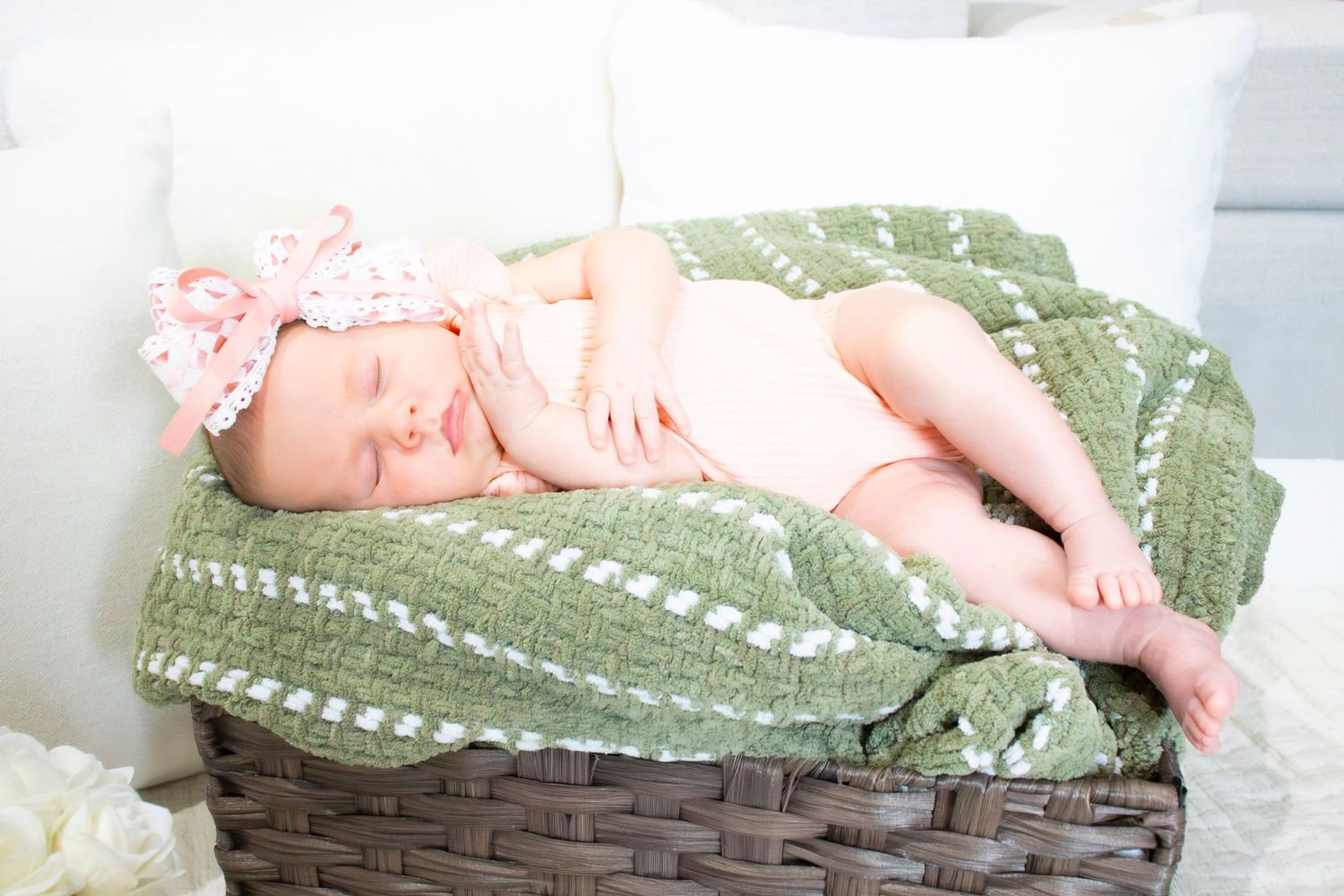 Sleeping newborn in a sage green blanket nestled in a woven basket lined with soft textiles.