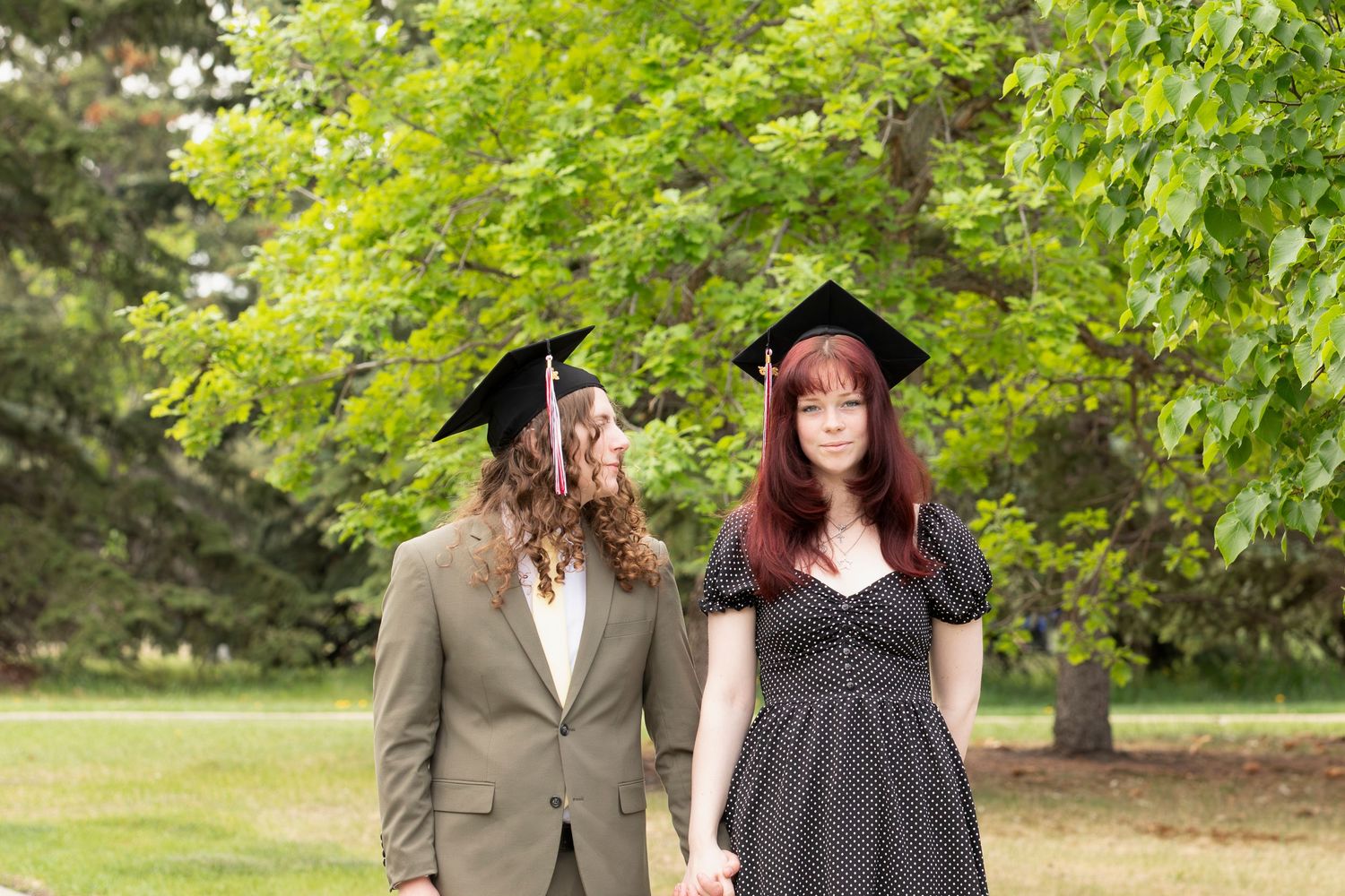 Two graduates sharing a moment together outdoors in graduation attire and casual dress.