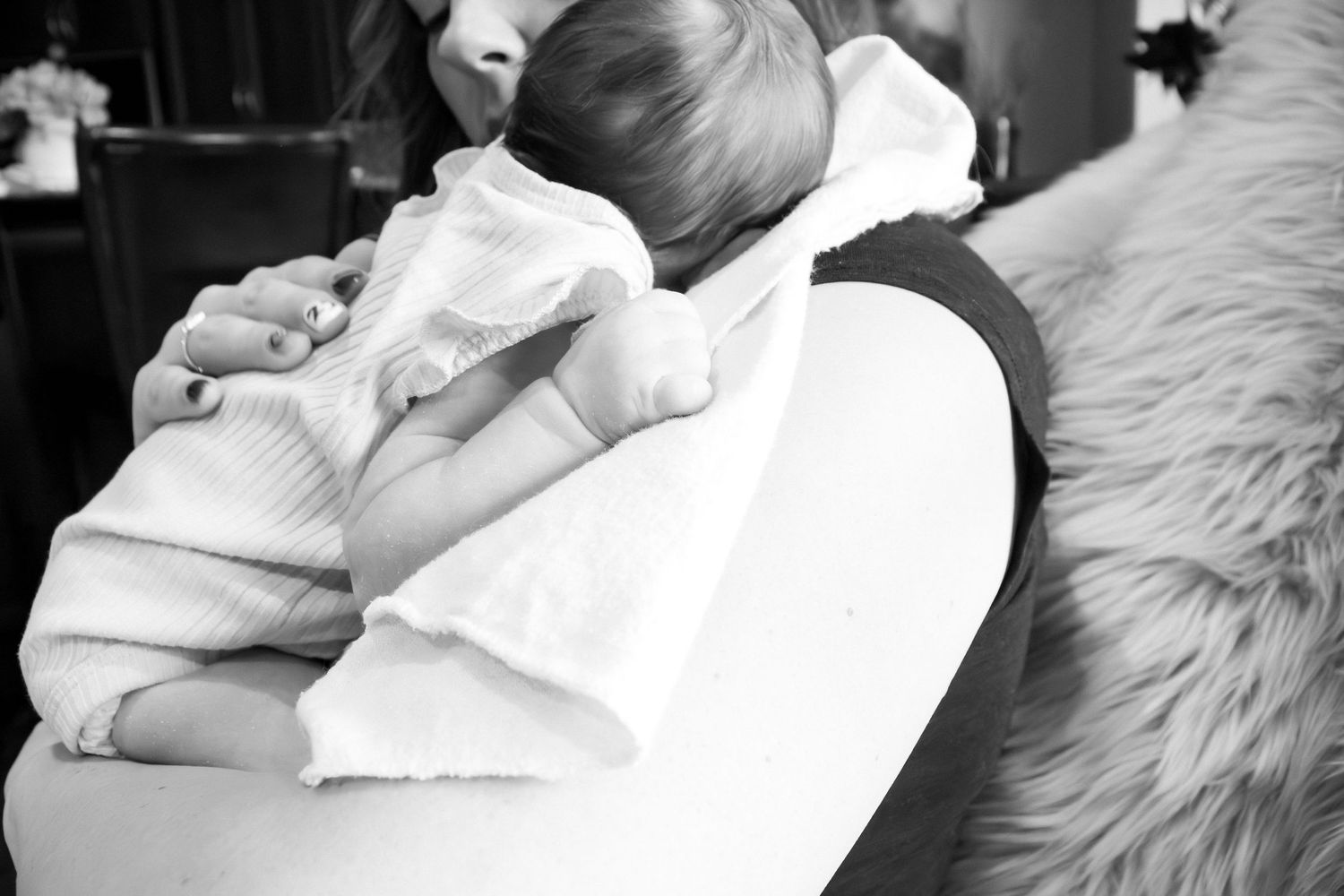 Newborn photography session with baby sleeping on white textured blanket in black and white.