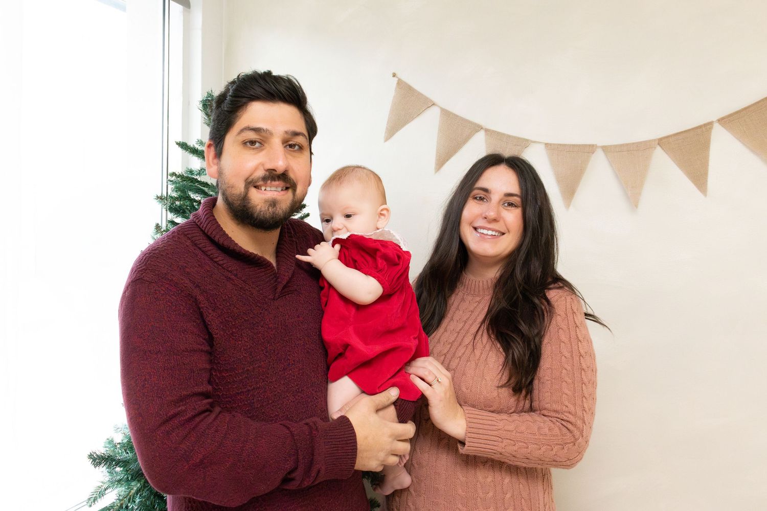 Family poses together with holiday decor and white bunting banners in background.