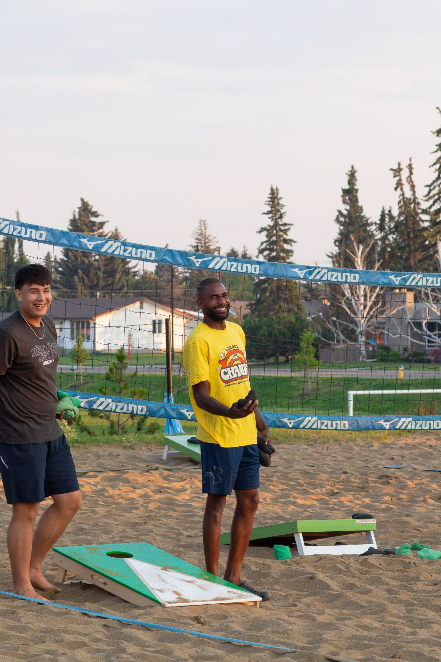 People playing cornhole on sandy beach court with blue banners in background.