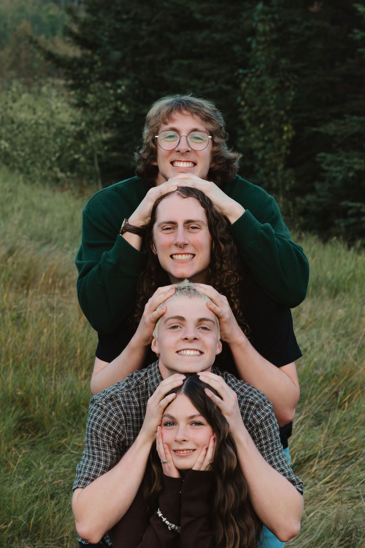 A playful couple poses together in a grassy field while wearing dark green and plaid clothing.