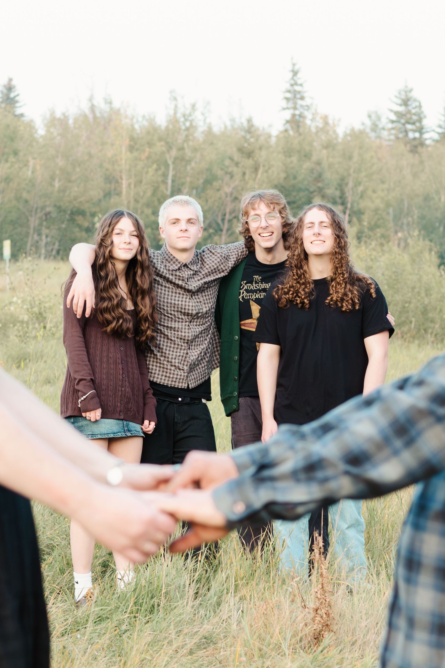 A group stands together in a grassy field wearing dark clothing while holding hands in a line.