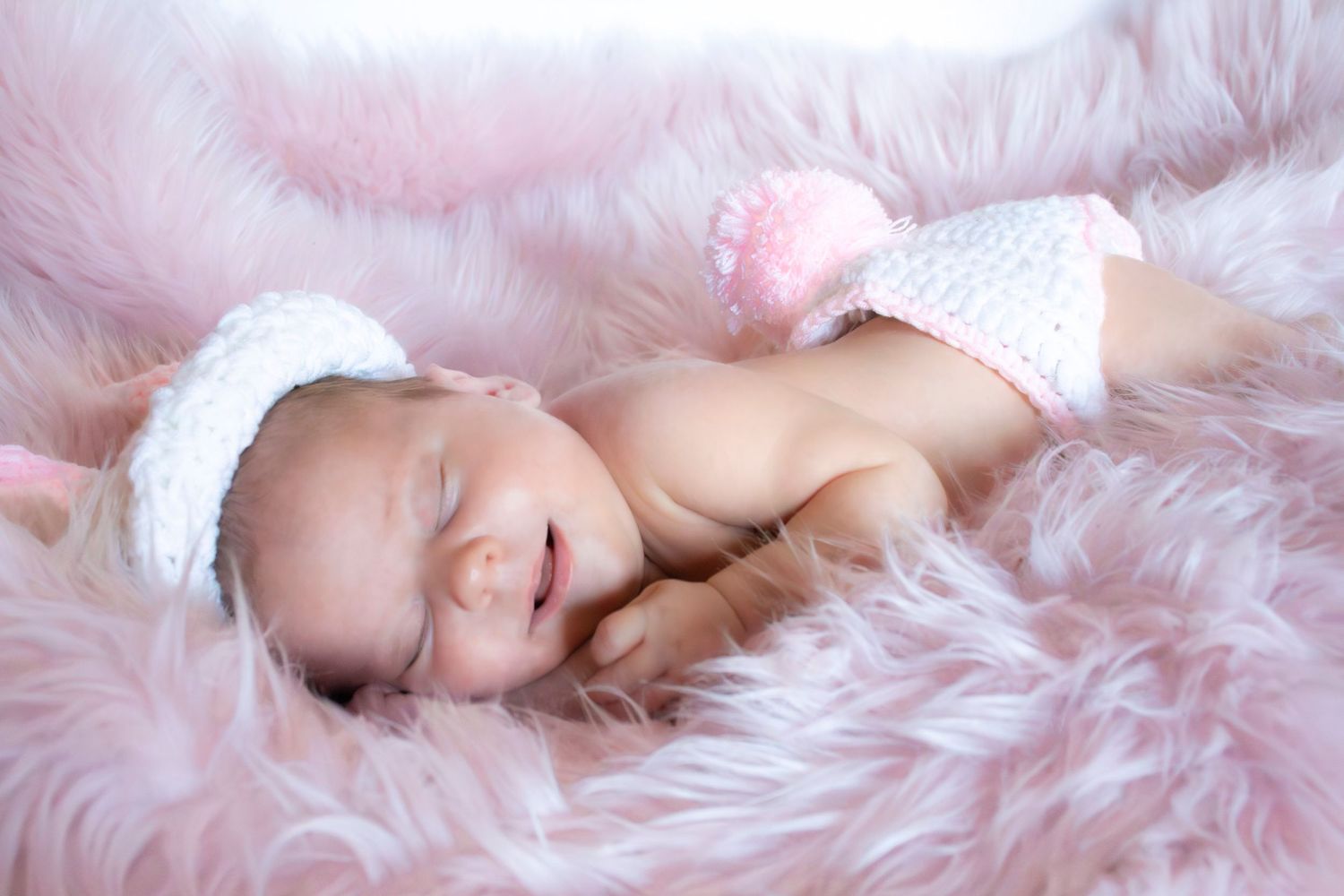 Baby sleeping peacefully on pink and white fur textured blanket.