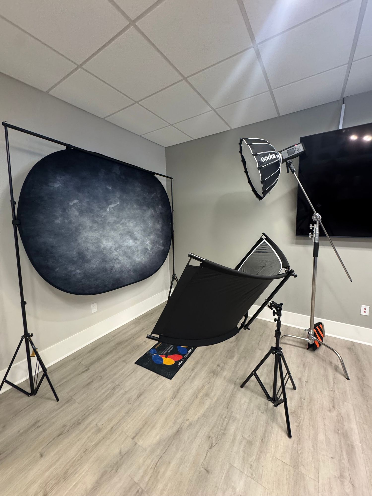 Professional photography studio setup with multiple light stands, reflectors and black backdrops in a bright room.