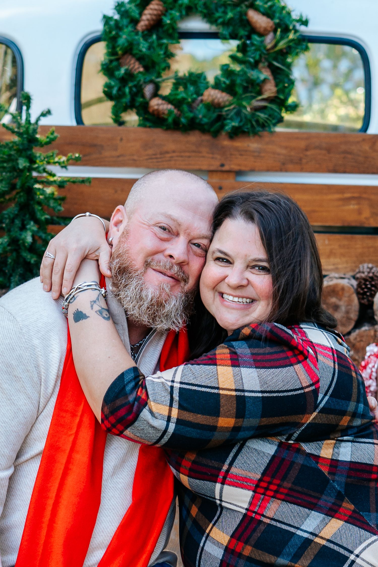 Couple cuddling on a wooden bench with holiday decor and plaid blanket.