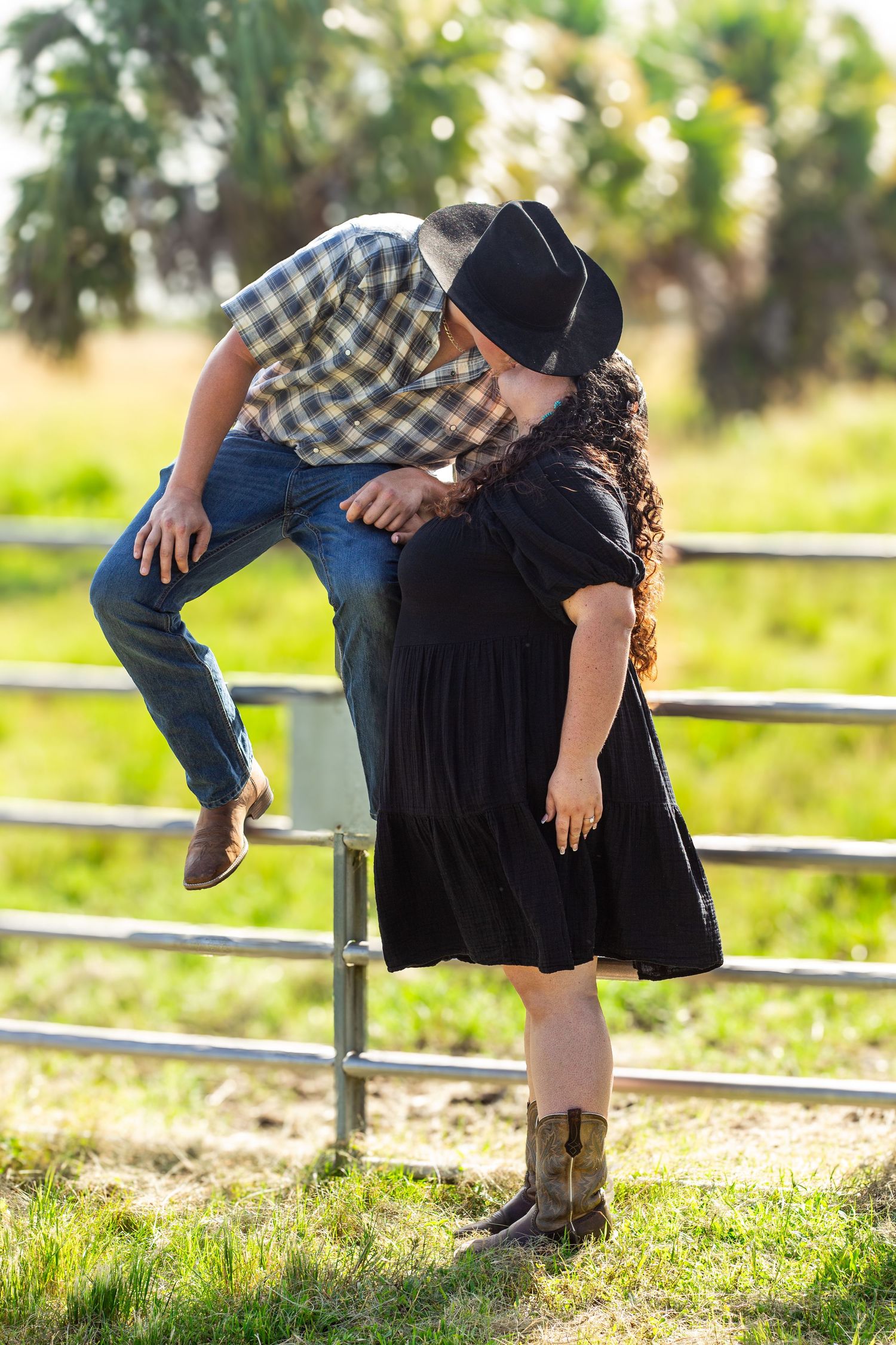 A playful couple poses on a wooden fence in a rustic outdoor setting.