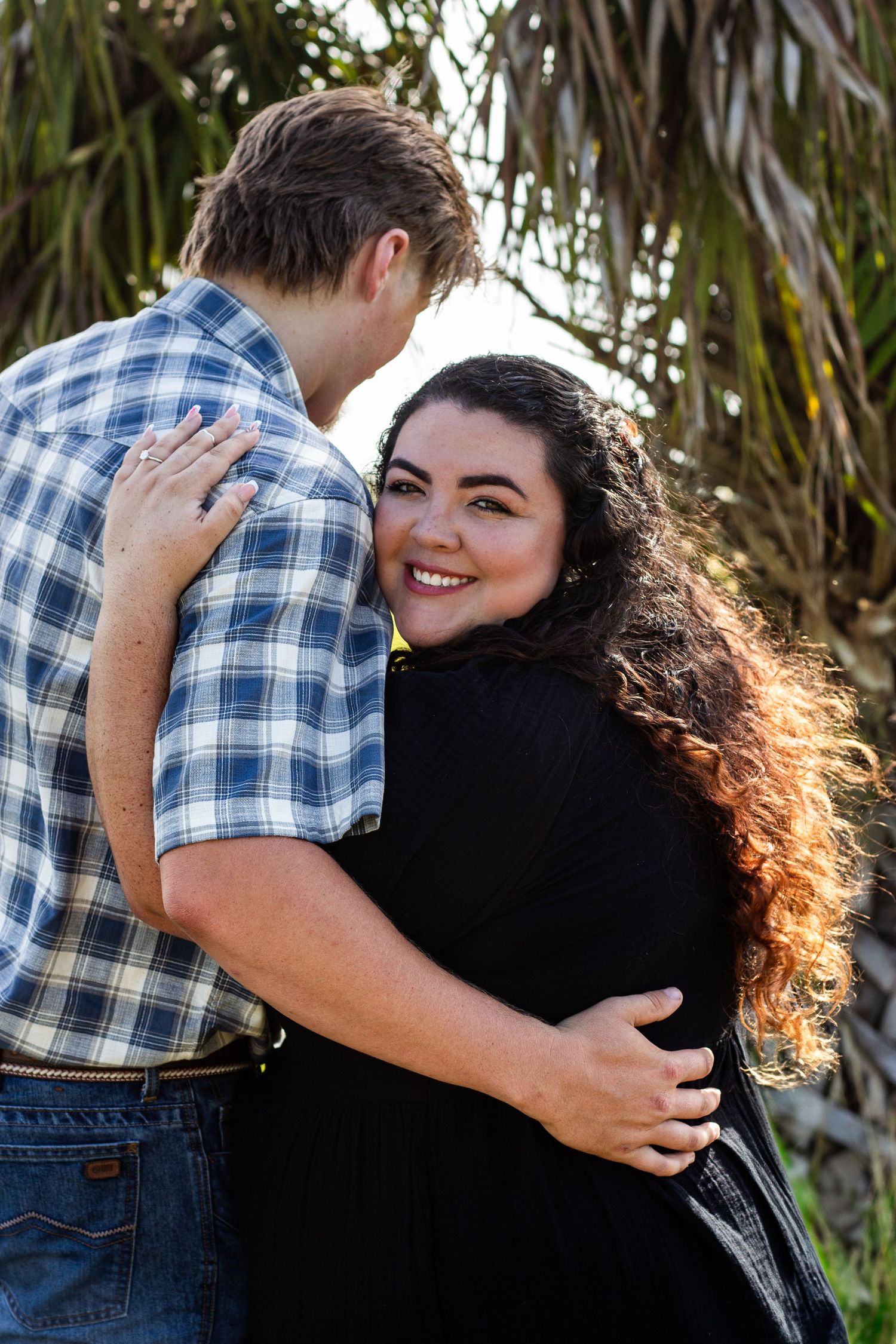 A couple shares a tender embrace against a backdrop of tropical foliage.