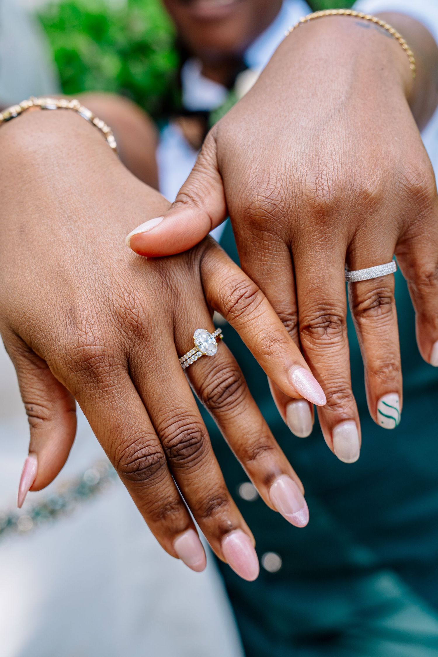 Couple displaying wedding rings, woman wearing diamond engagement ring with pink nails, man wearing silver band, close-up shot.