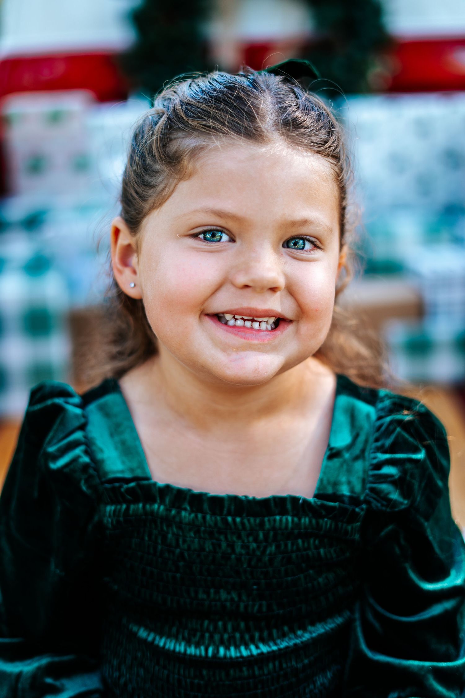 A young child wearing an emerald green velvet dress smiles brightly at the camera.