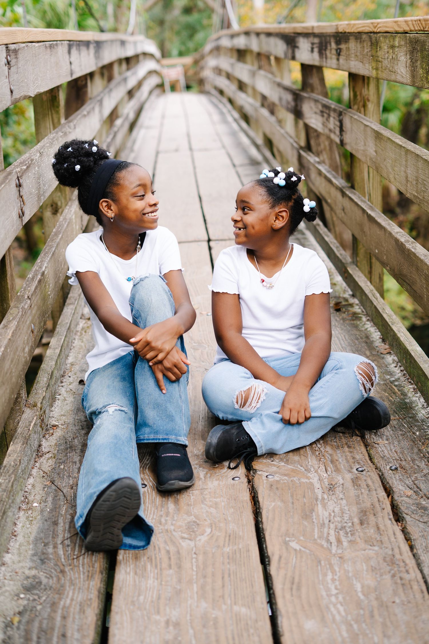Two people sitting and laughing together on a wooden boardwalk in casual attire.