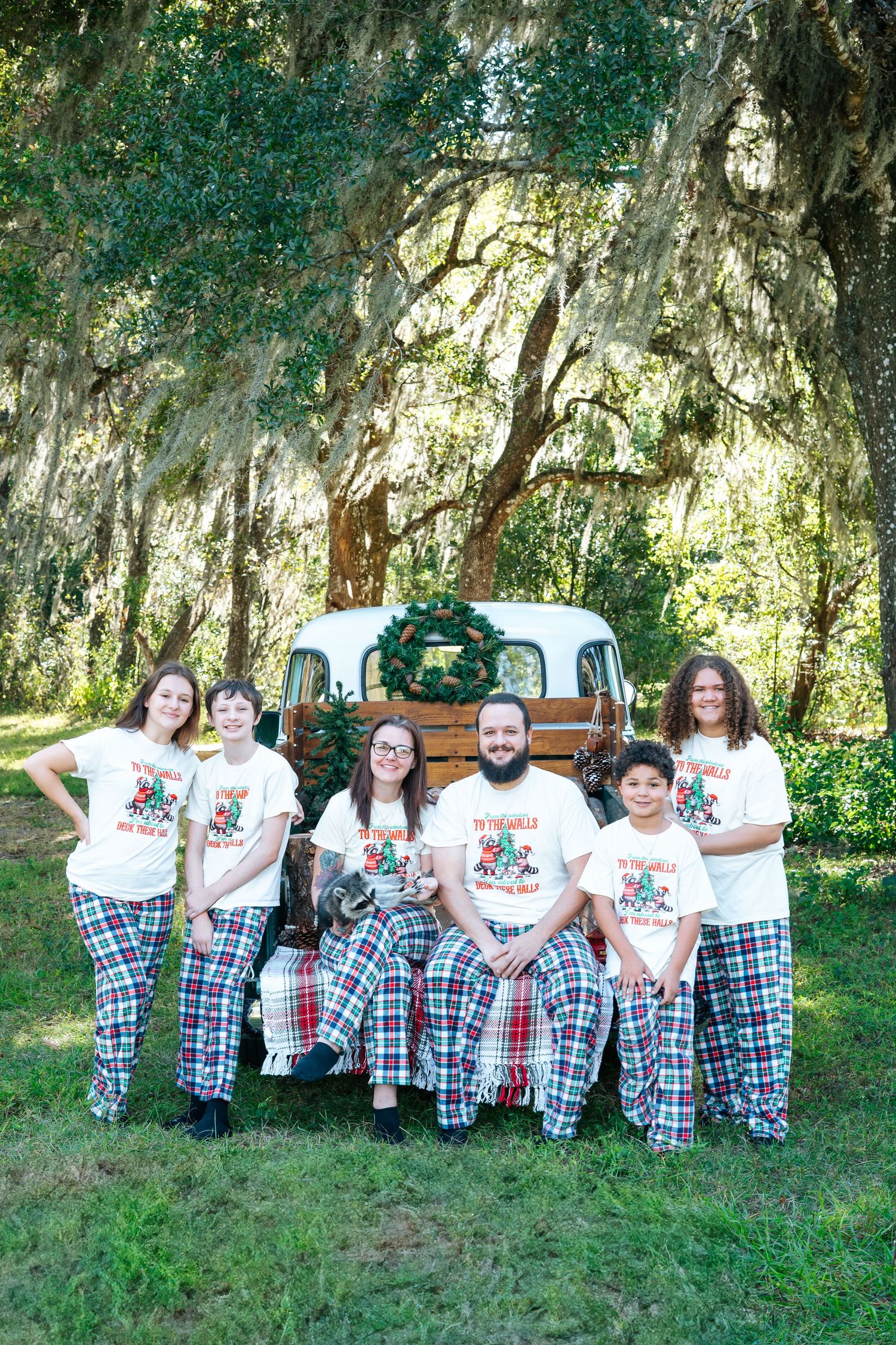 Family wearing matching holiday pajamas poses outdoors on grassy lawn.