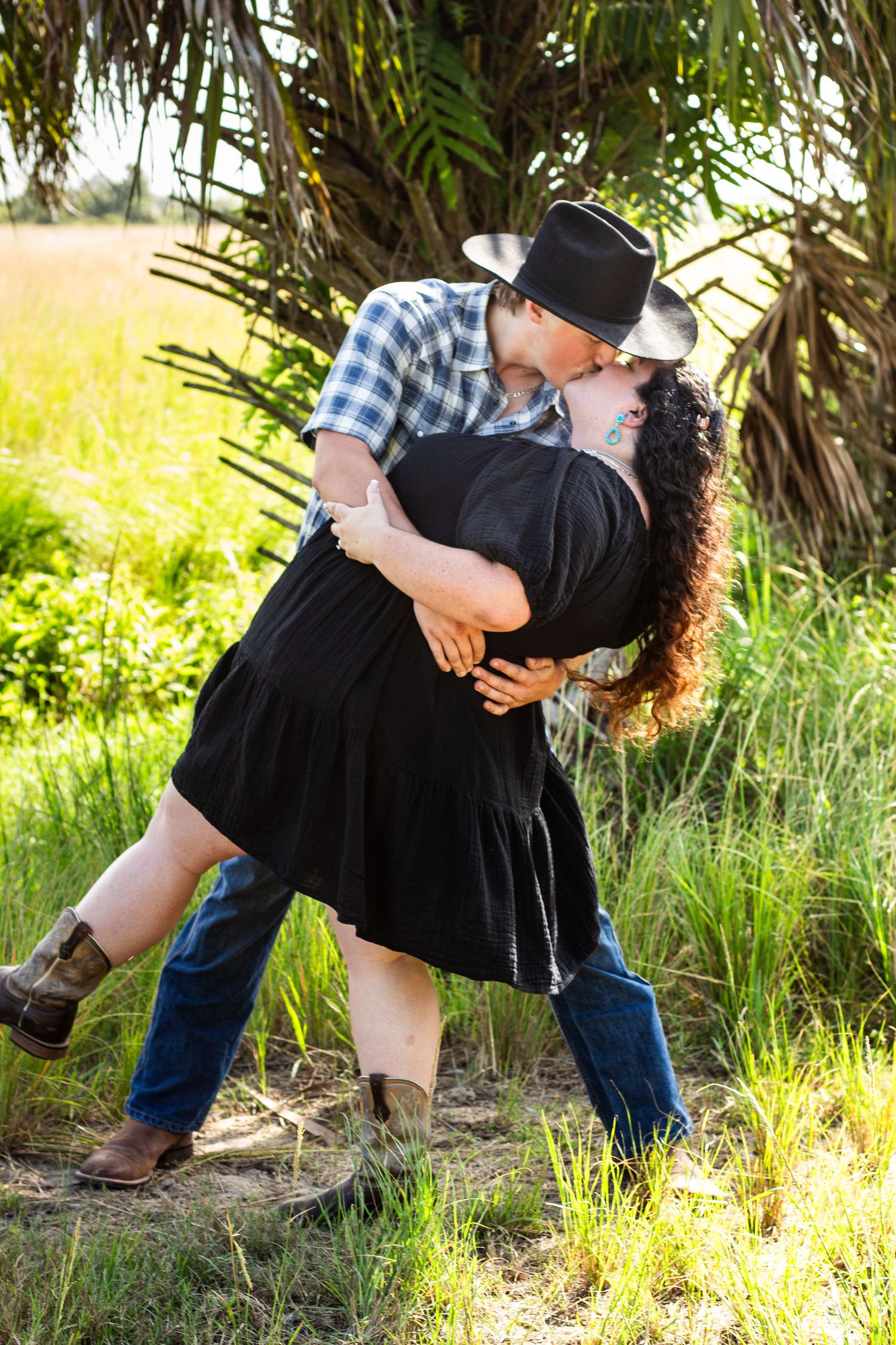 A romantic dip pose captured in a natural setting with palm trees in the background.