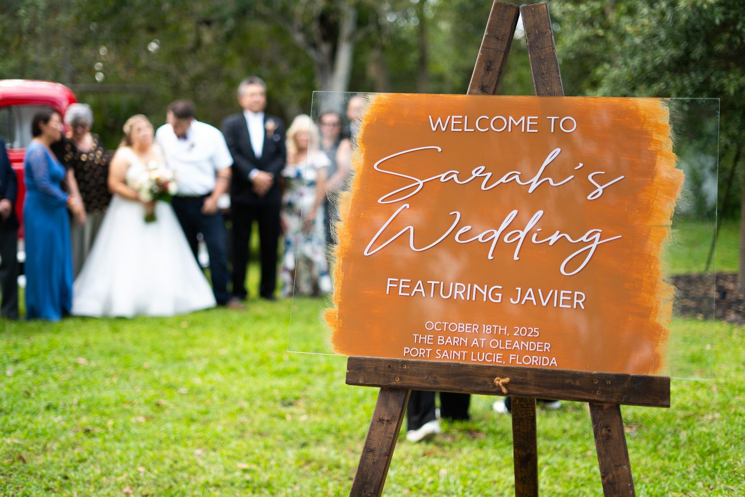 A wooden welcome sign for a wedding ceremony displayed in an outdoor garden setting.