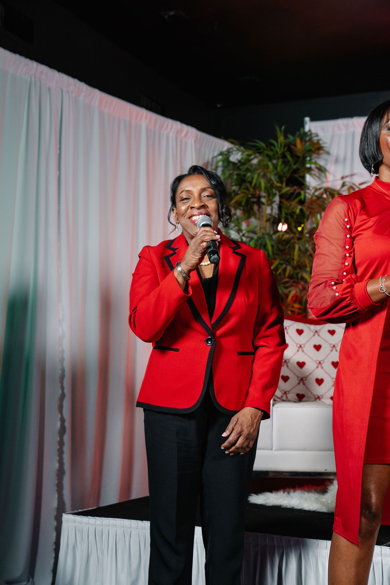 Woman in red blazer speaking into microphone on stage at a heart health awareness event.