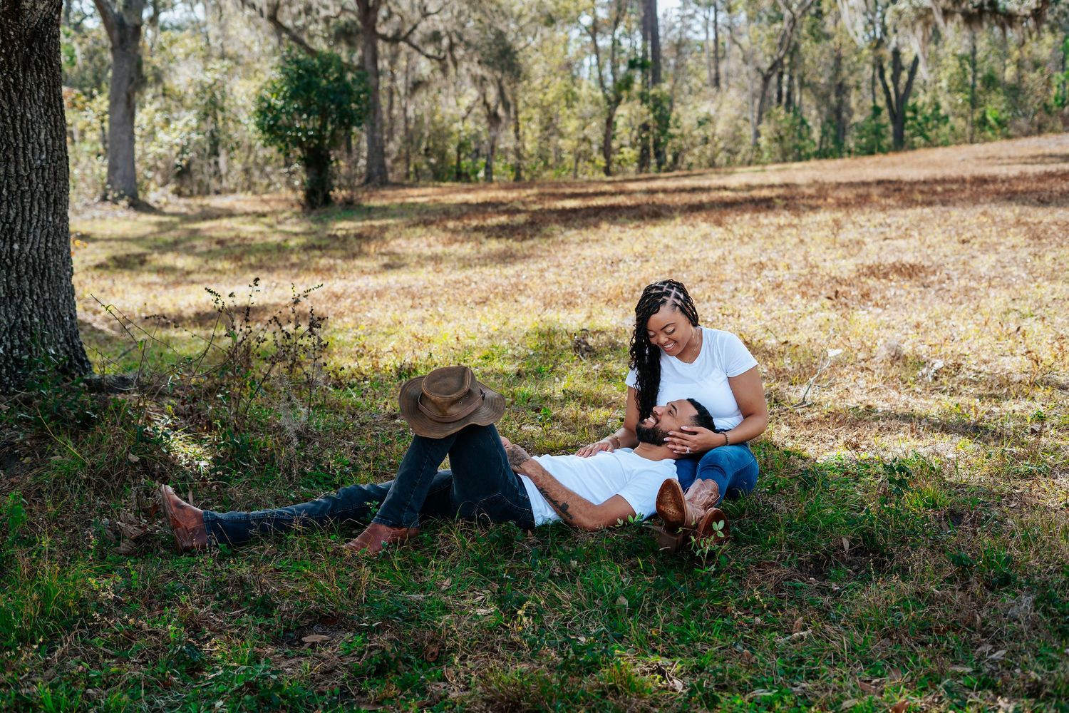 Couple relaxing outdoors in a wooded park, woman lying in mans lap on green grass surrounded by trees.