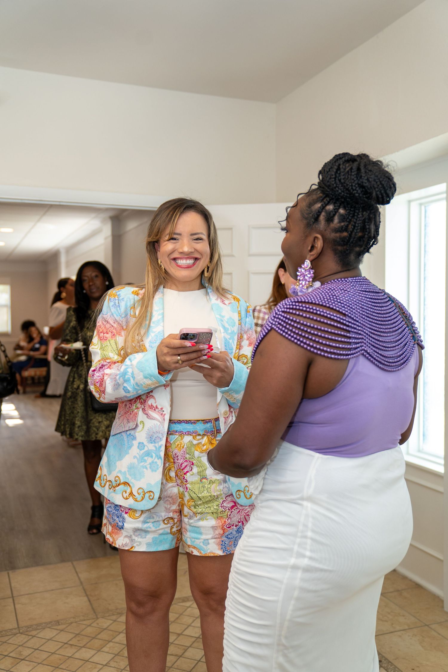 Two women smiling and conversing at an indoor social gathering event.