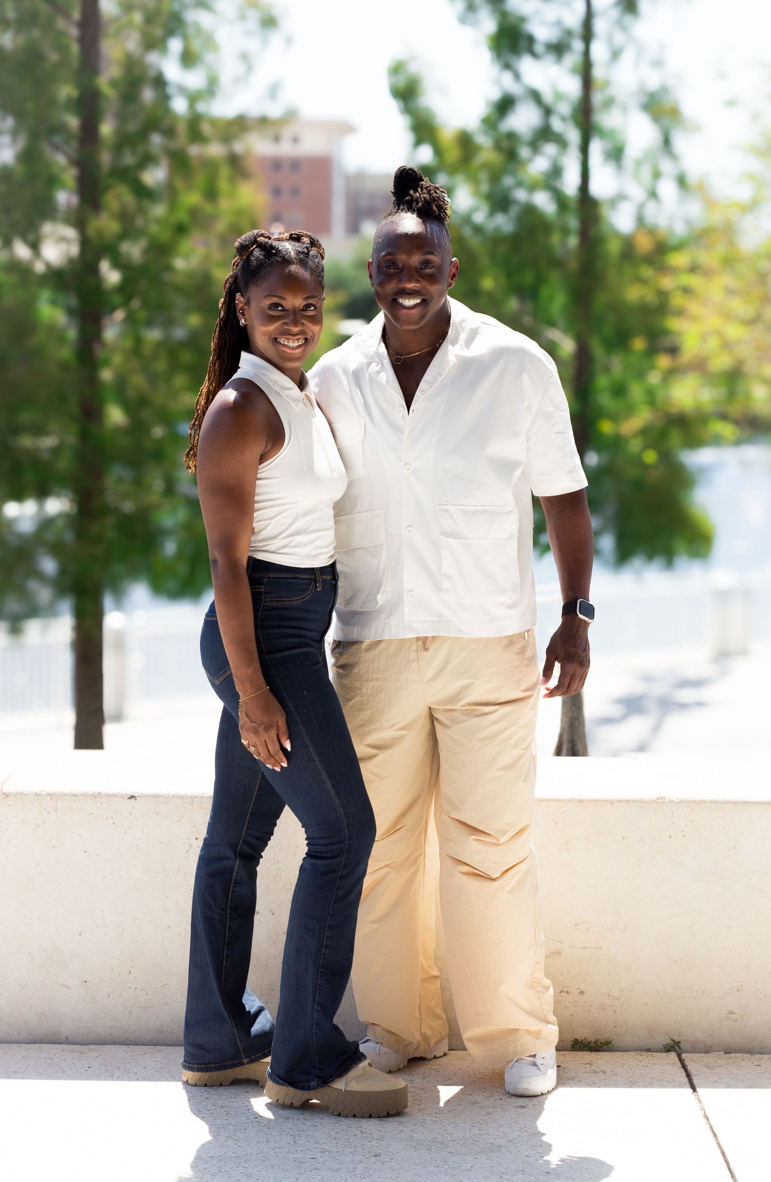 A couple in coordinated casual outfits shares laughter while sitting on a white wall outdoors.