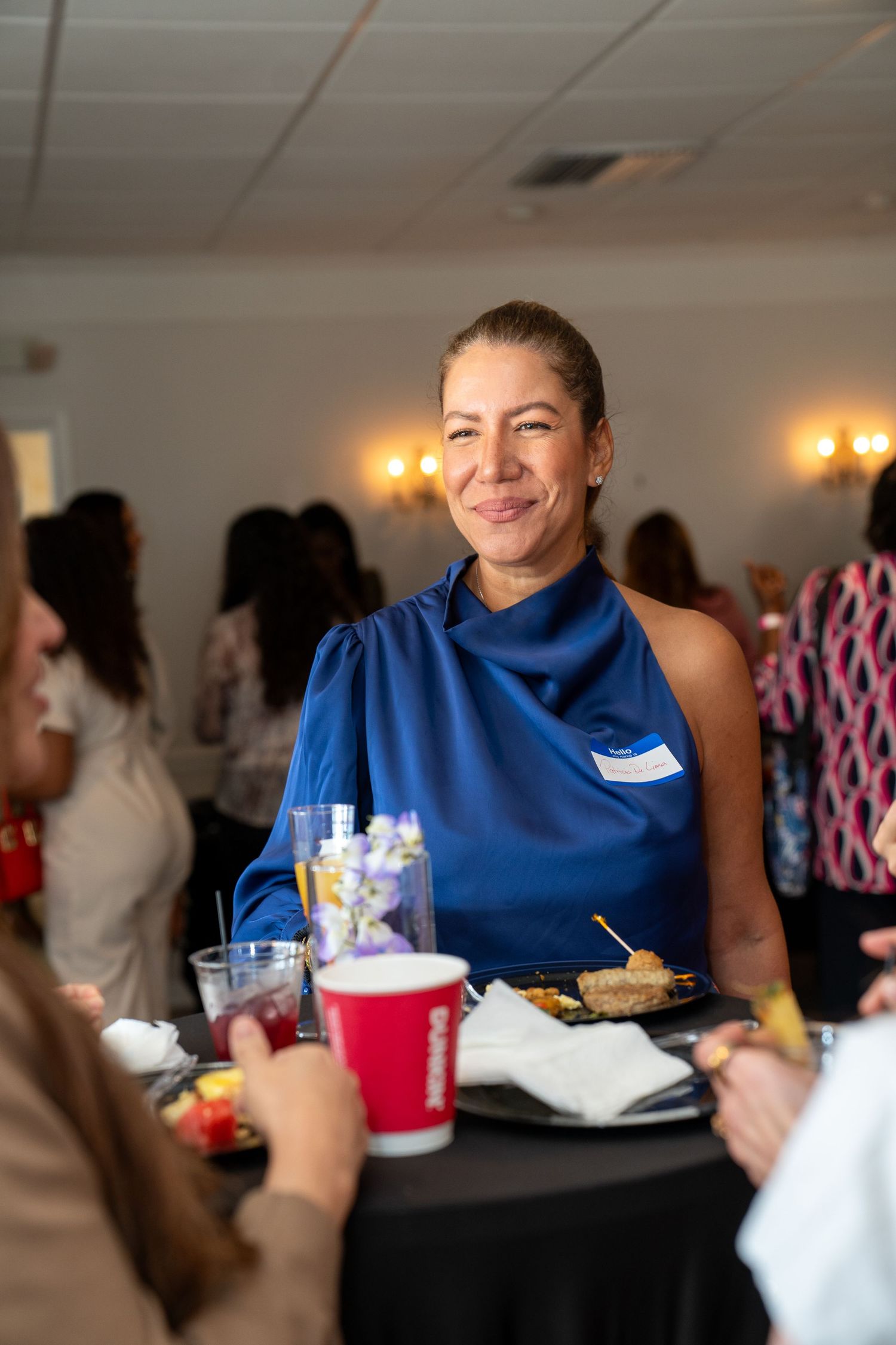 Woman in blue dress smiling at networking event with food and drinks on table.