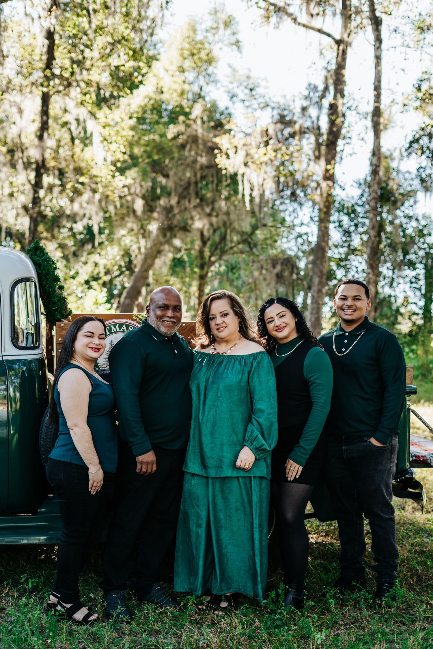 Family in matching green and black outfits posed together by a vintage truck.